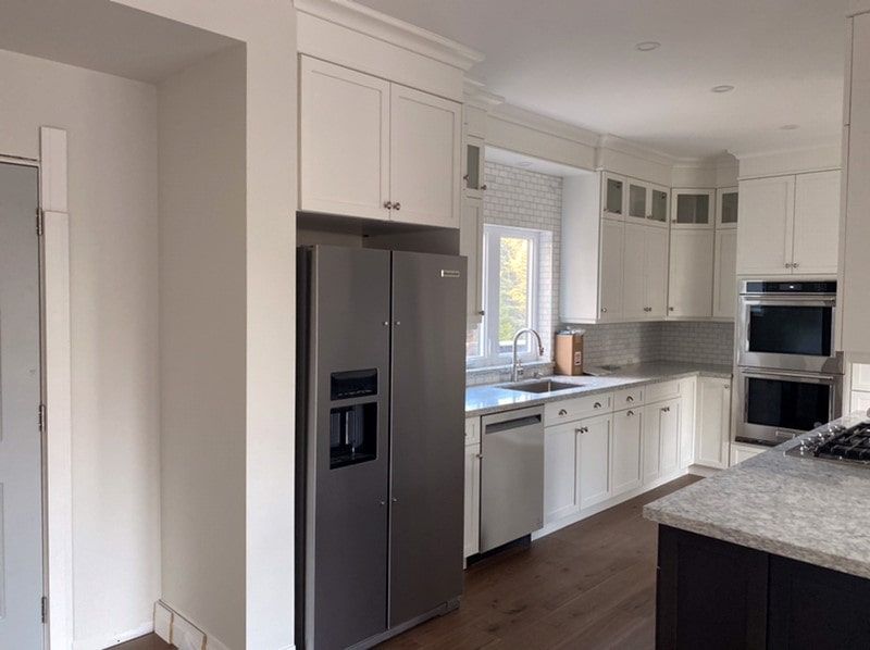 Modern white kitchen with stainless steel appliances, granite countertops, and hardwood floors.