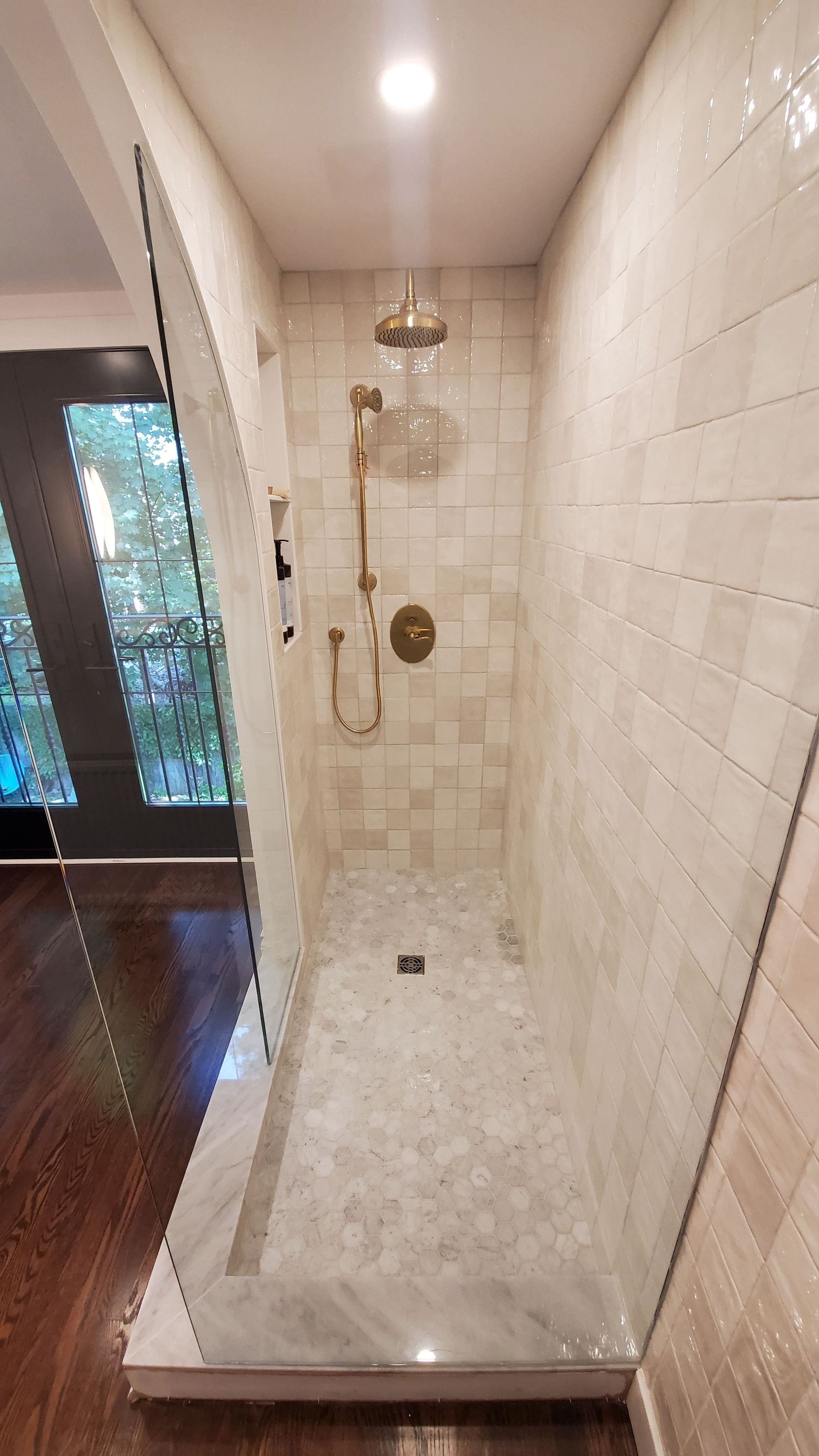 Shower with tan and cream tiles, gold fixtures, and glass door.