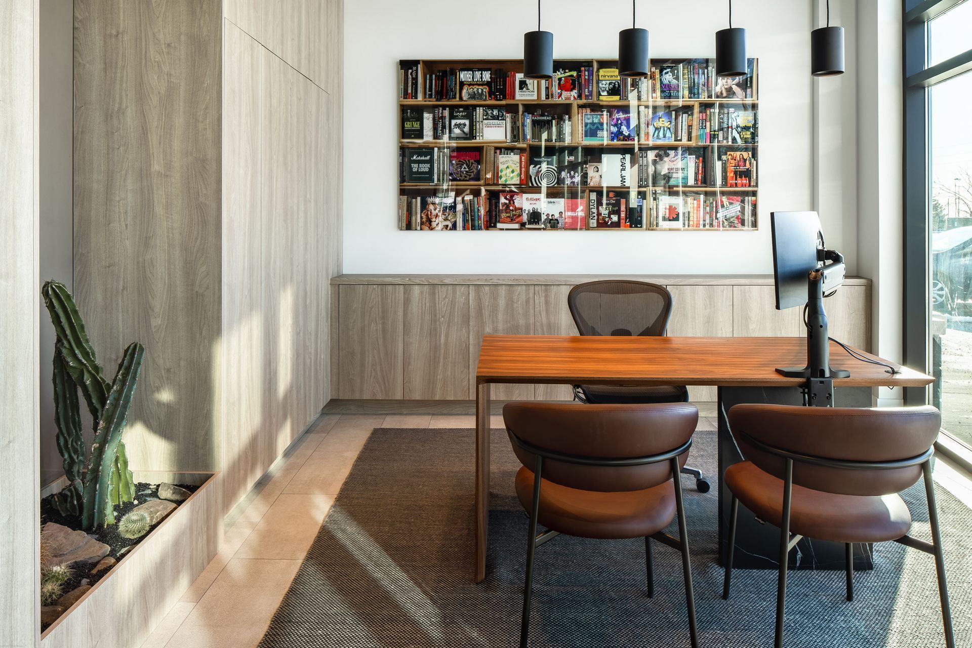 Office with wooden desk, brown chairs, built-in shelving, bookcase art, and hanging black lights.