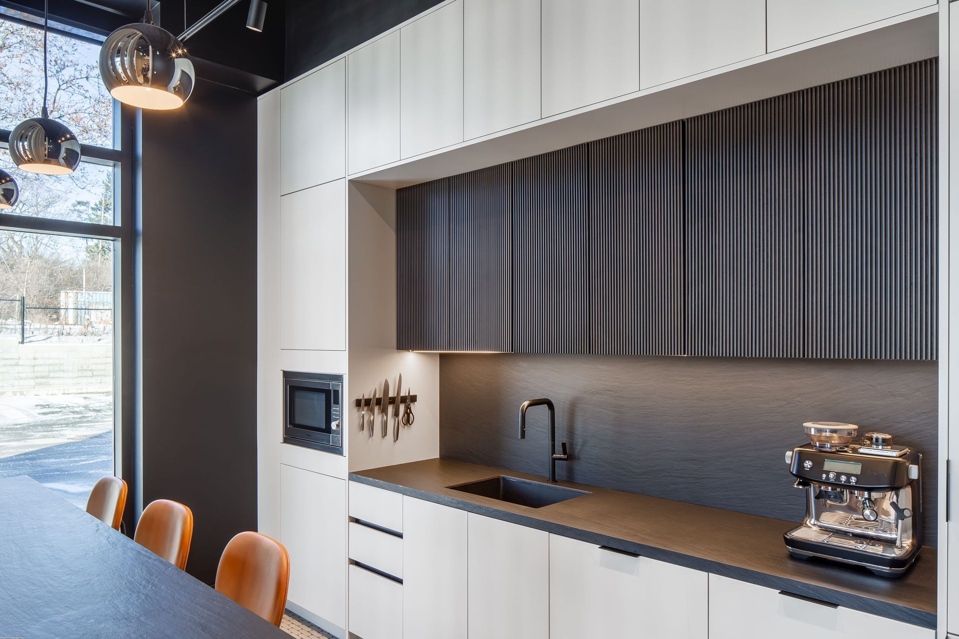 Modern kitchen with light wood cabinets, dark backsplash, and coffee machine.