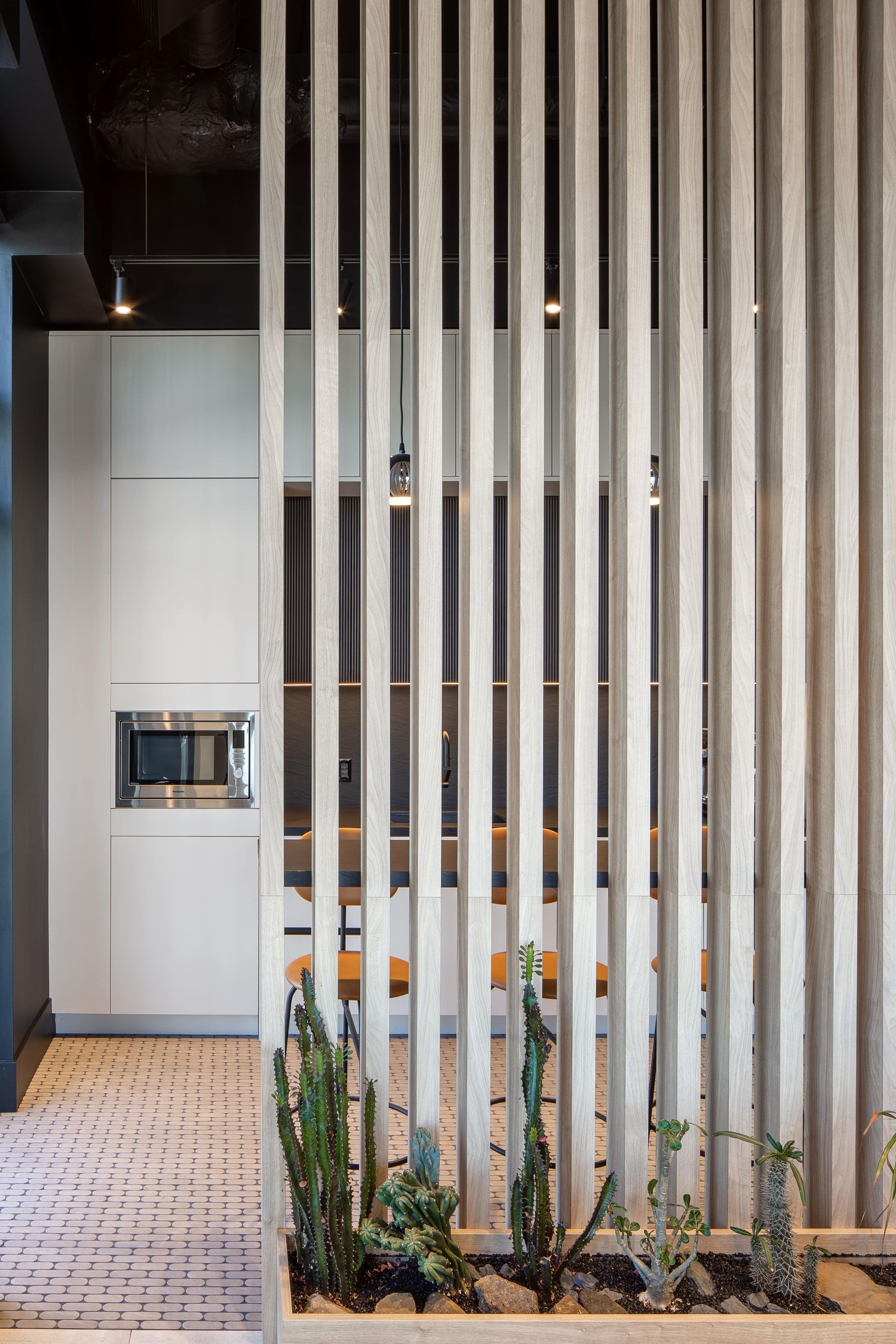 Slatted gray partition with potted plants in front, opening to a modern interior space.