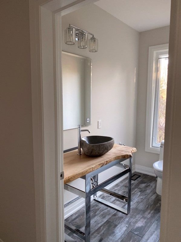 Bathroom with gray walls, wood vanity, vessel sink, chrome faucet, and window with white curtain.