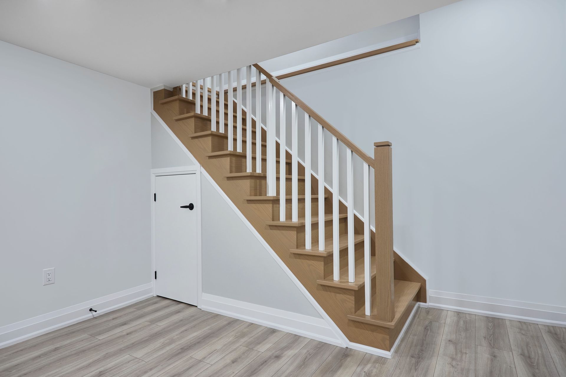 Staircase with wooden steps and white railing in a room with light-colored flooring and walls, and a small door.