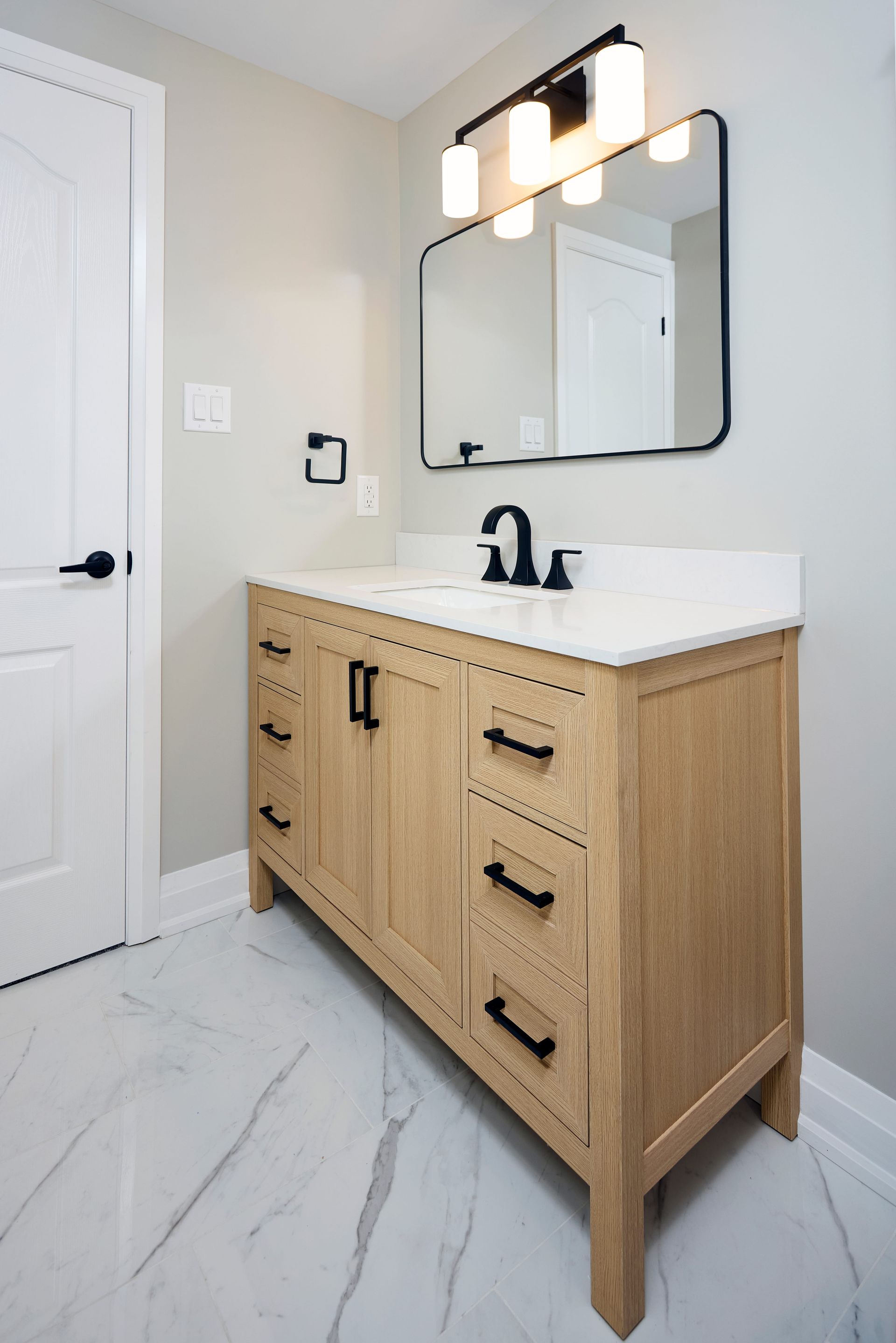 Bathroom with a wooden vanity, marble countertop, black fixtures, and a rectangular mirror.
