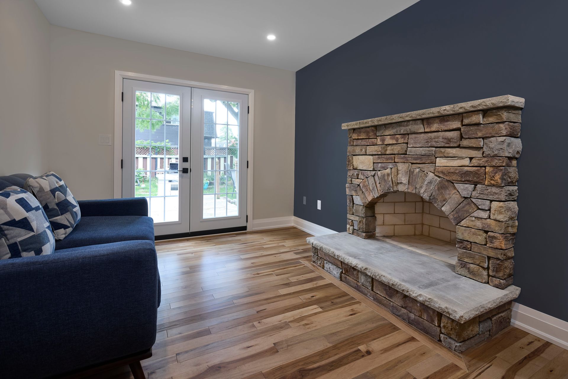 Living room with stone fireplace, blue sofa, and French doors to outdoors; hardwood floors.