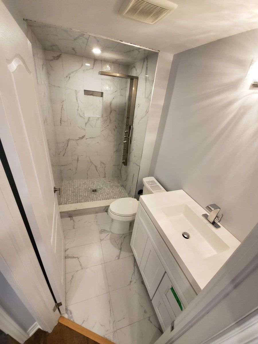 Small bathroom with white marble tile shower and flooring; white vanity, toilet and pale blue walls.