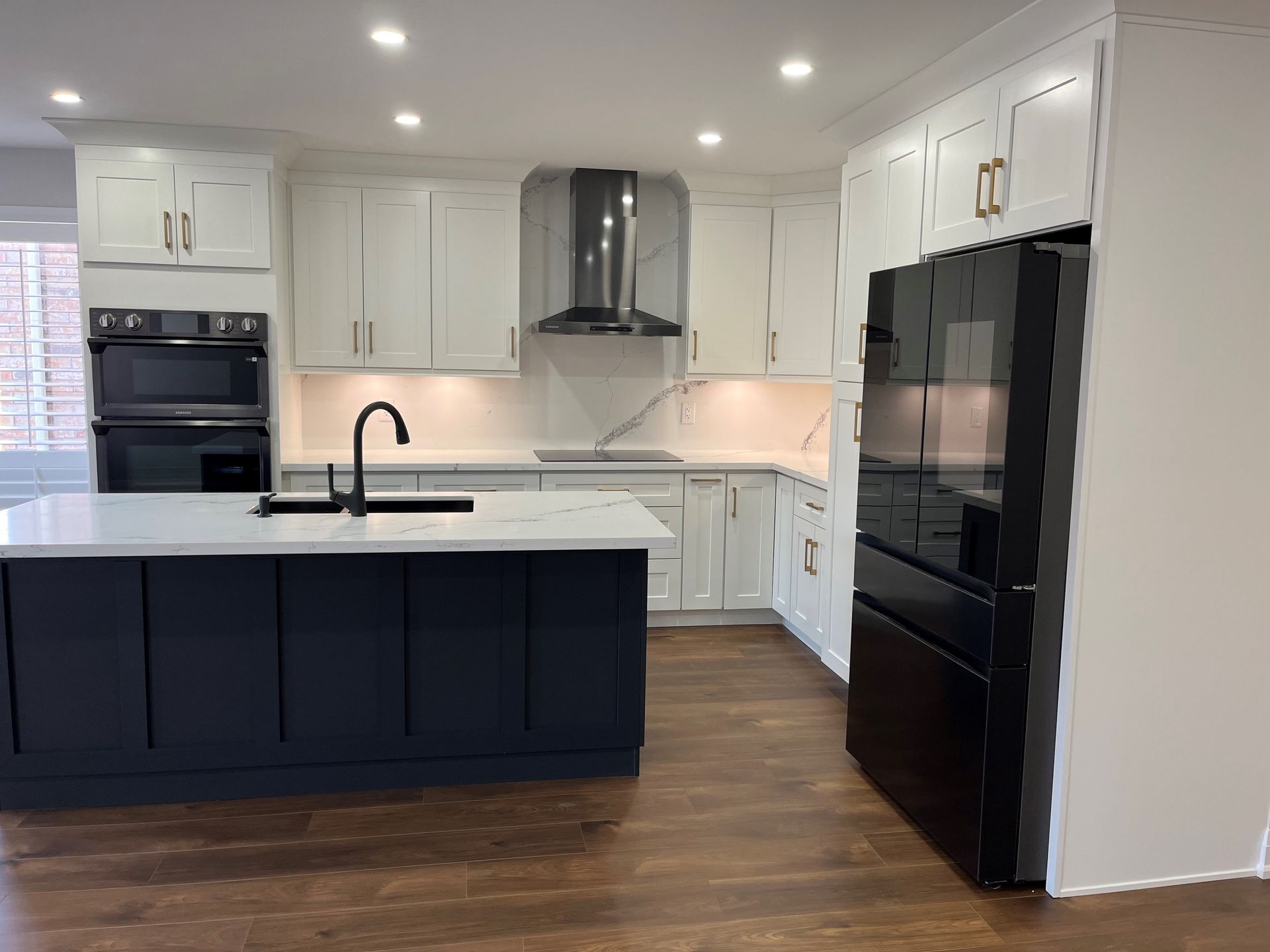 Modern kitchen with white cabinets, dark blue island, black appliances, and marble countertops.