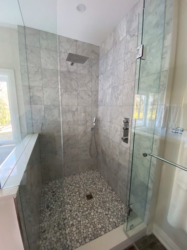 Shower with pebble floor, gray tiled walls, glass door, and chrome fixtures.