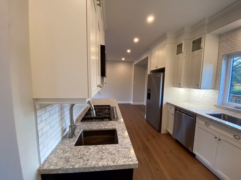 Modern kitchen with white cabinets, stainless steel appliances, and wood flooring.