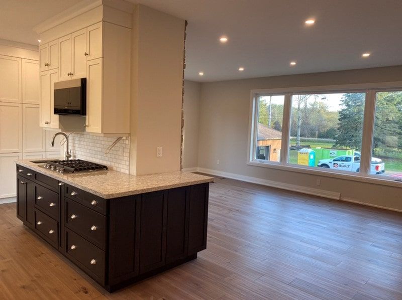 Kitchen with brown and white cabinets, island with stovetop, and large window with outdoor view.