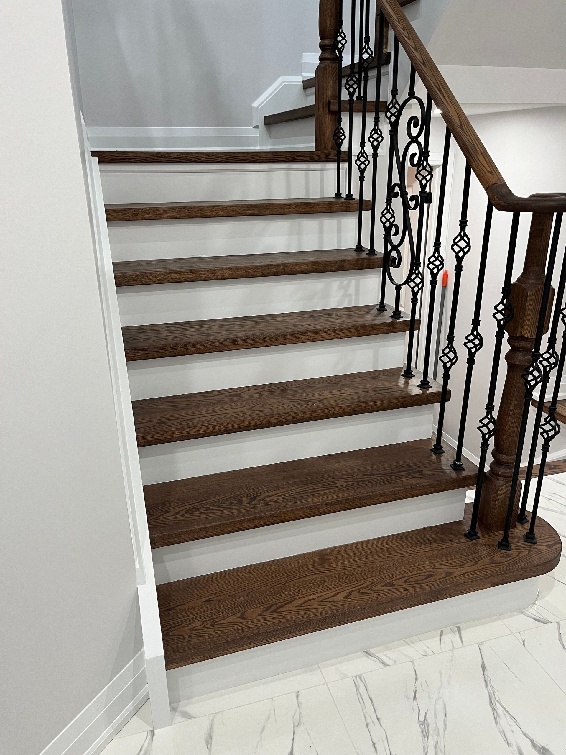 Wooden staircase with white risers, dark wood treads, and wrought iron railing.