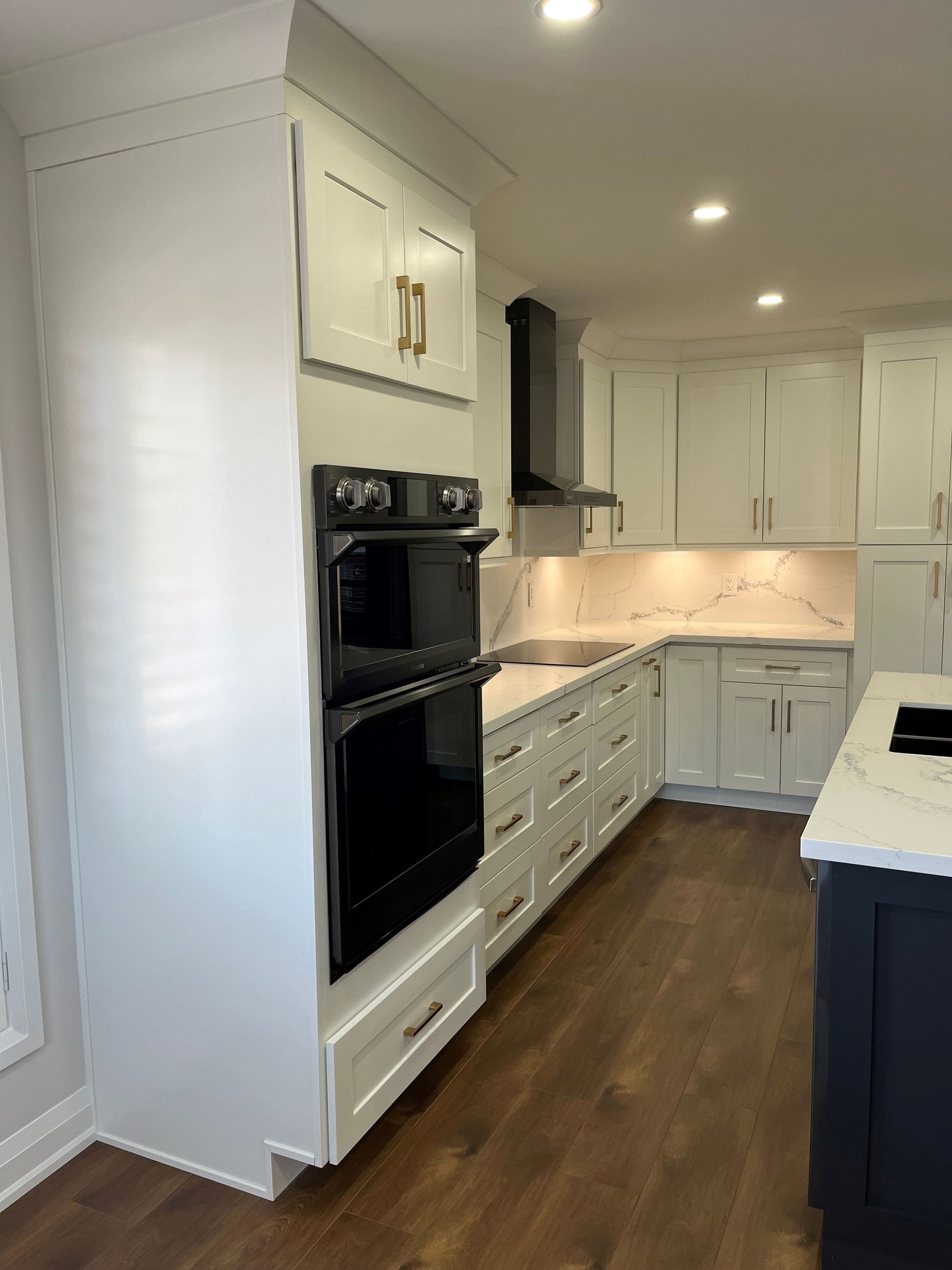 White kitchen with built-in oven and cabinets, dark wood floor, marble countertops.