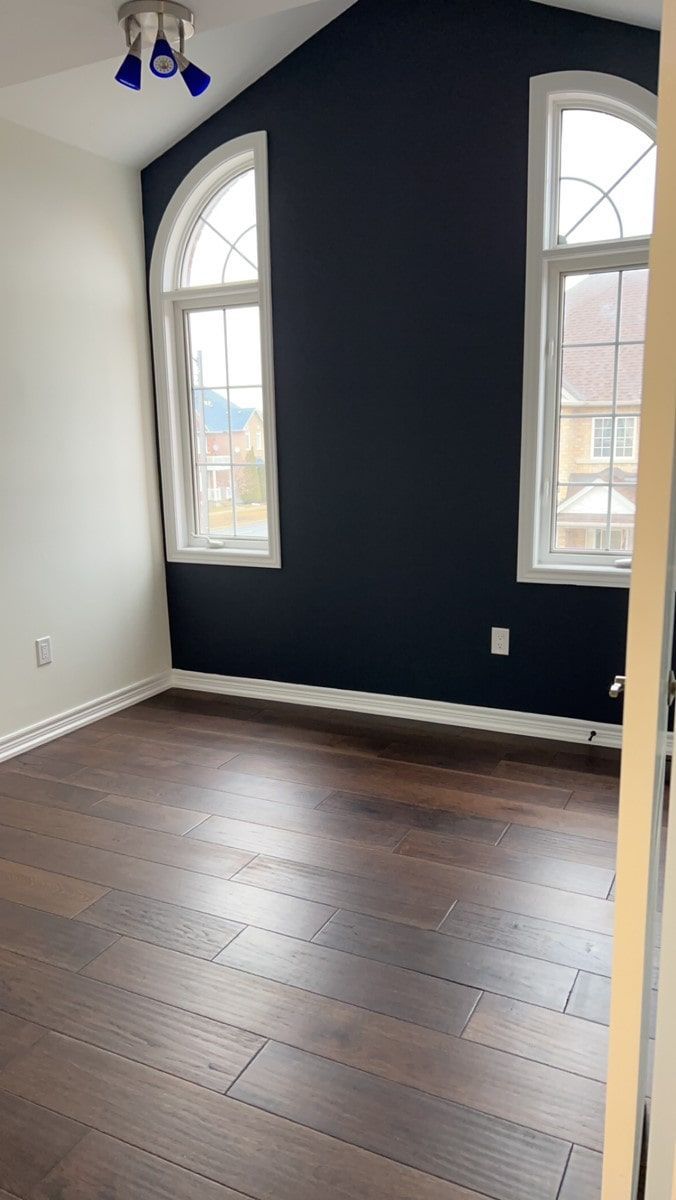 Empty room with dark wood floors, white walls, and a black accent wall with two arched windows.