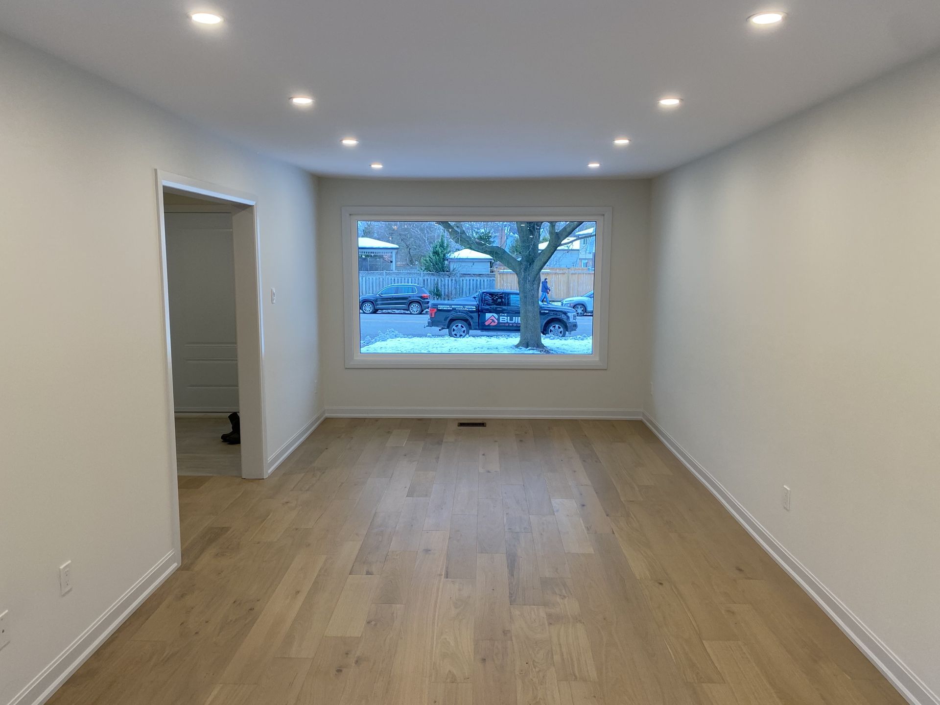 Empty, bright room with hardwood floor, recessed lighting, and a large window.