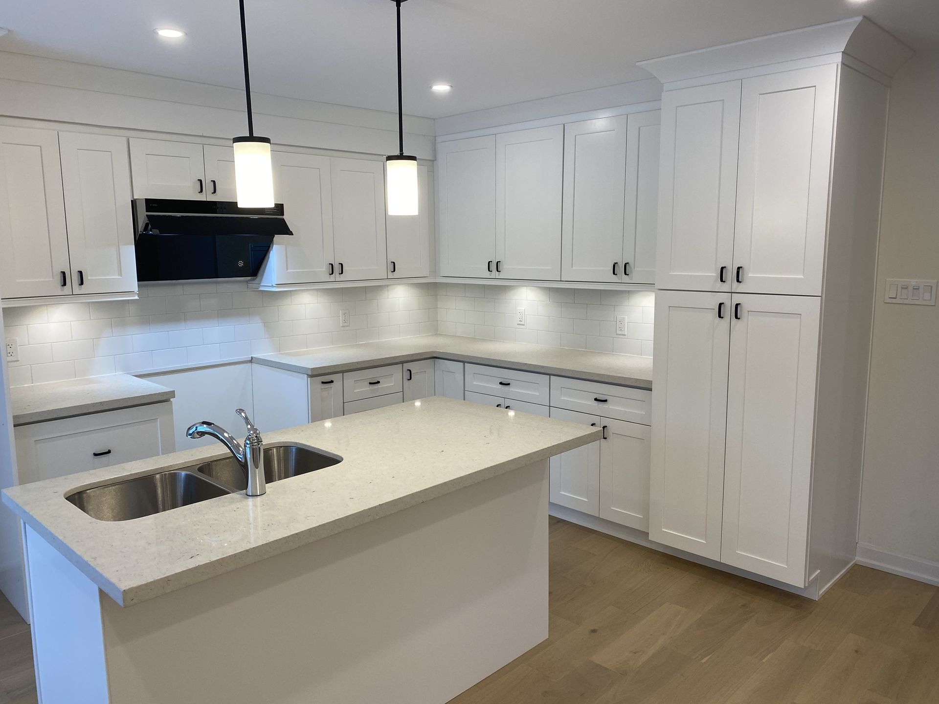 White kitchen with island, cabinets, countertops, and two pendant lights.