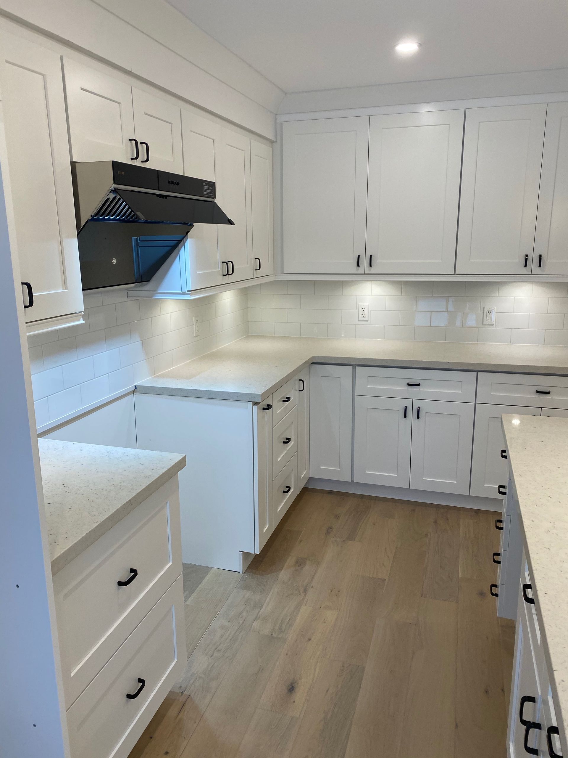 White kitchen with cabinets, countertops, and stainless steel range hood. Light wood floor.