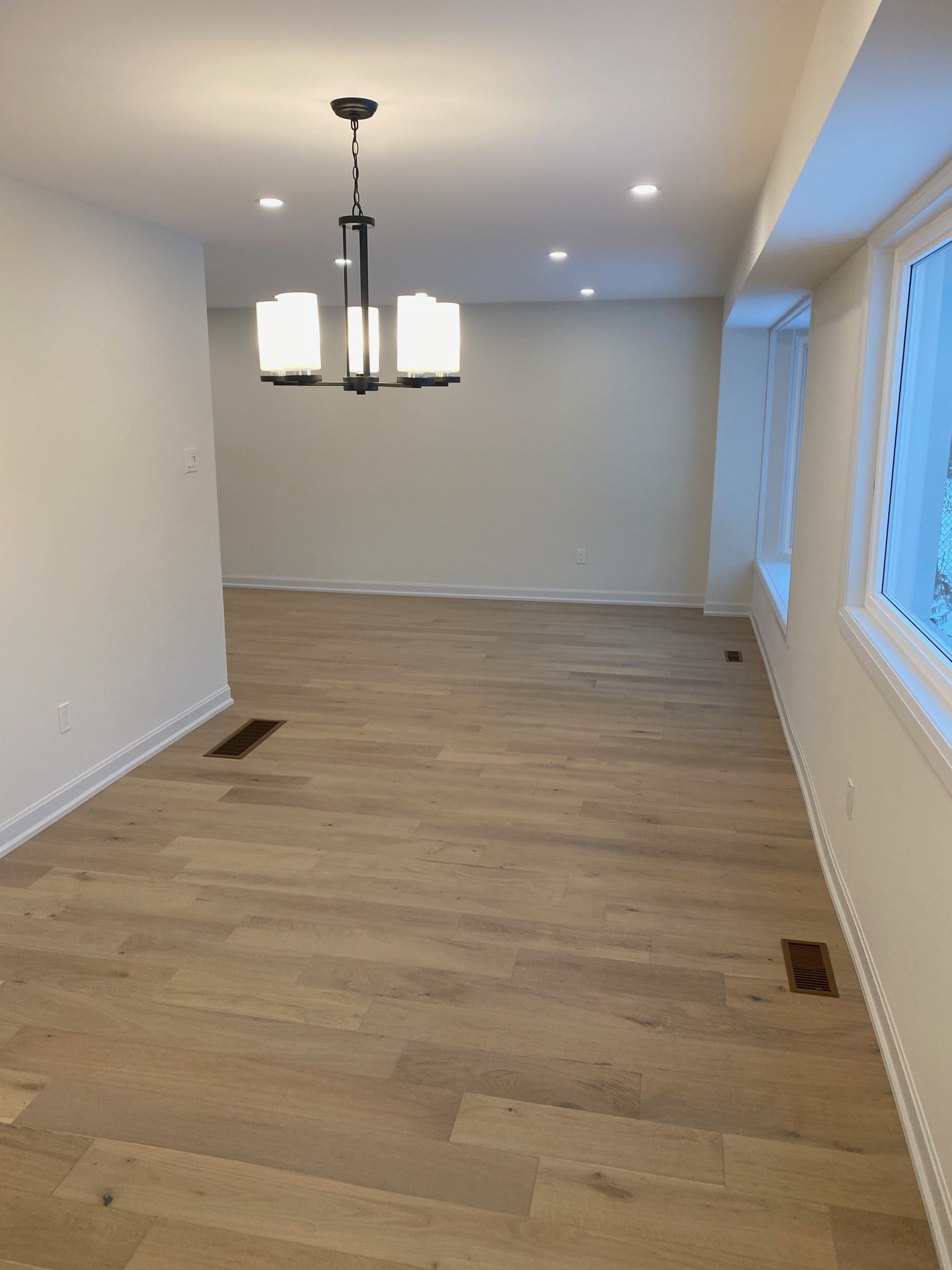 Empty dining room with wood flooring, white walls, and a chandelier.
