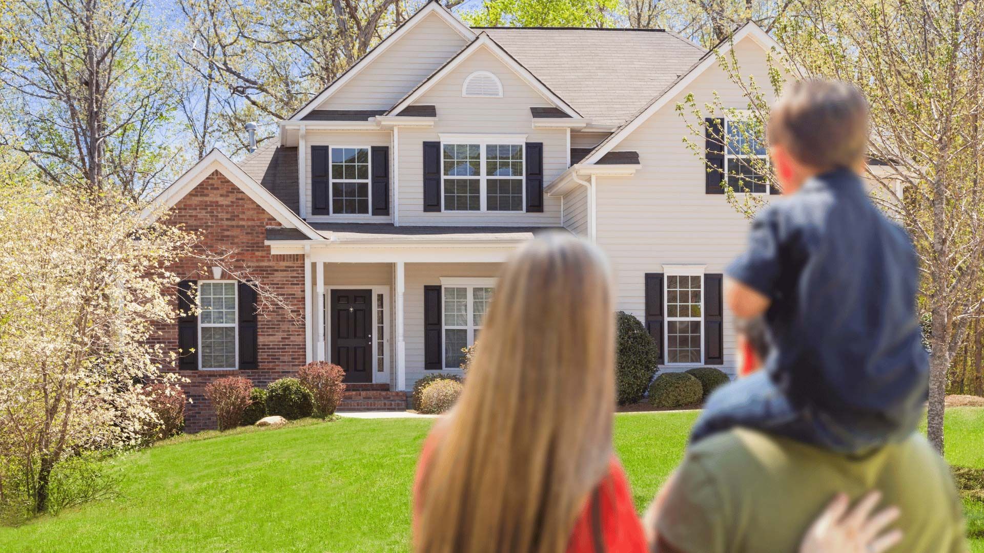 Family looking at a two-story suburban house with a brick exterior and green lawn