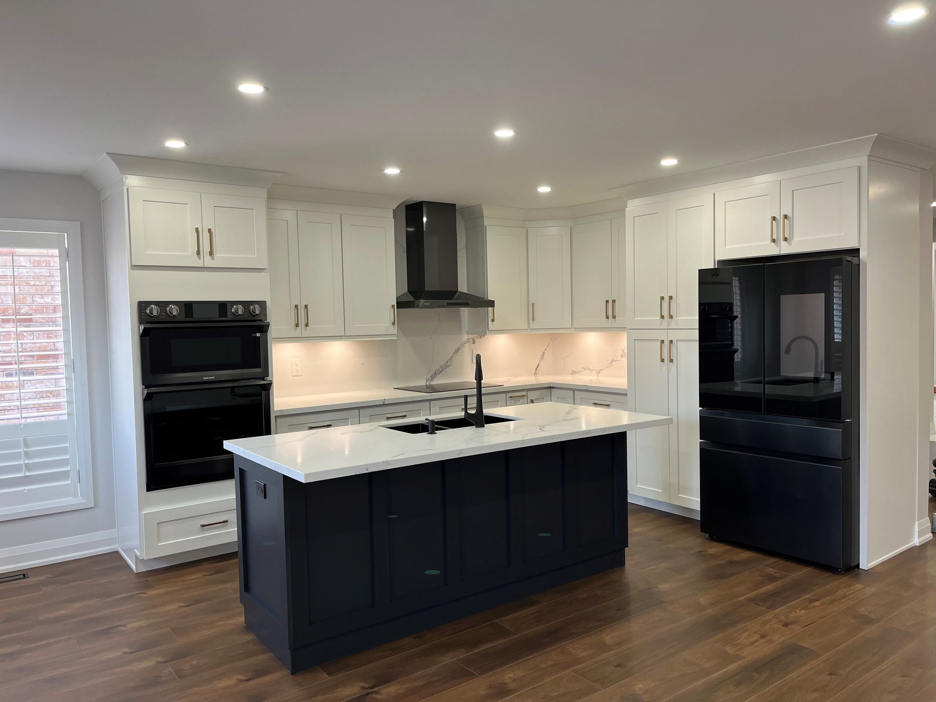 Modern kitchen with white cabinets, dark island, black appliances, and hardwood floors.