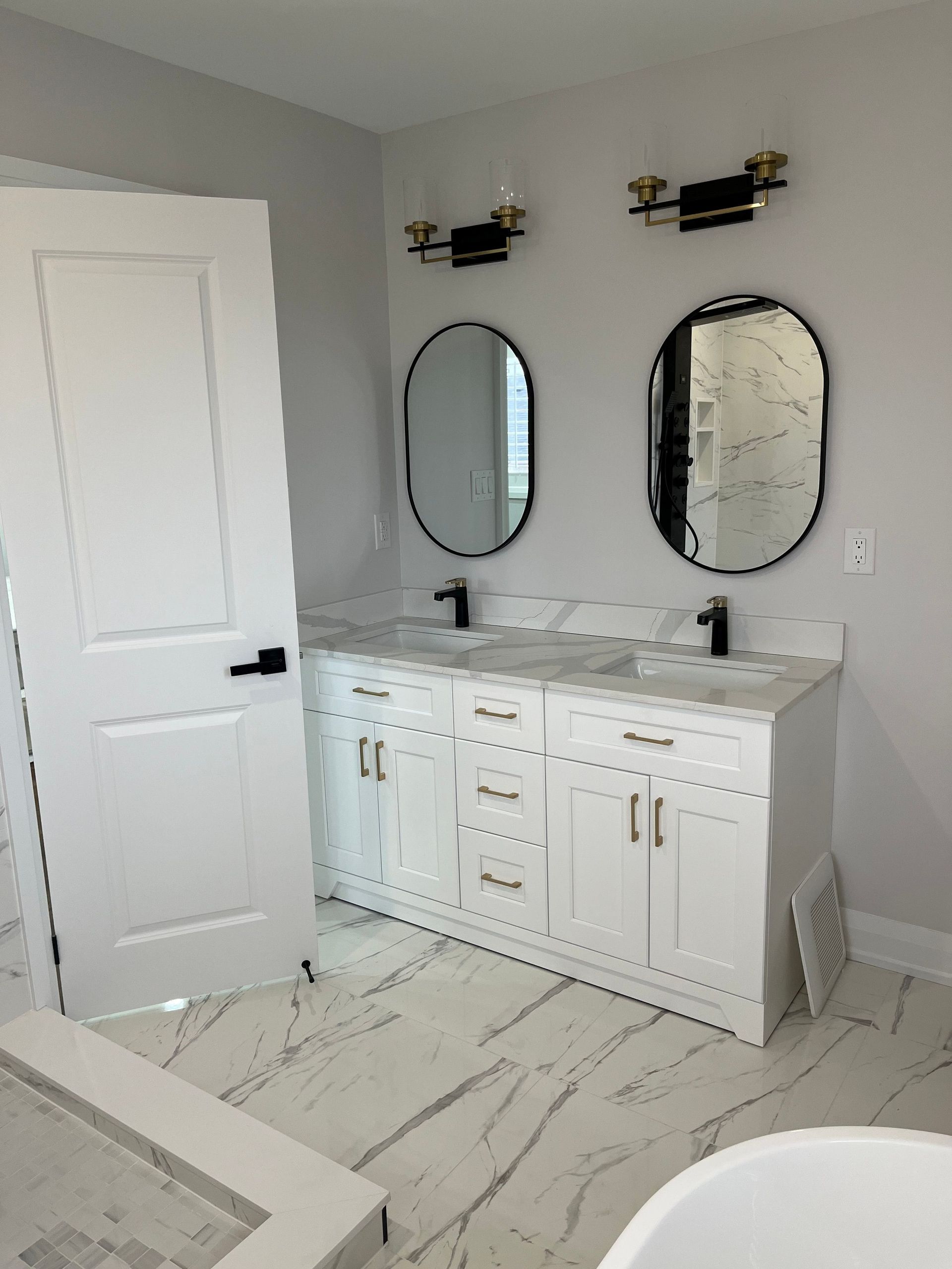 White bathroom vanity with two oval mirrors, black fixtures, and gold hardware.