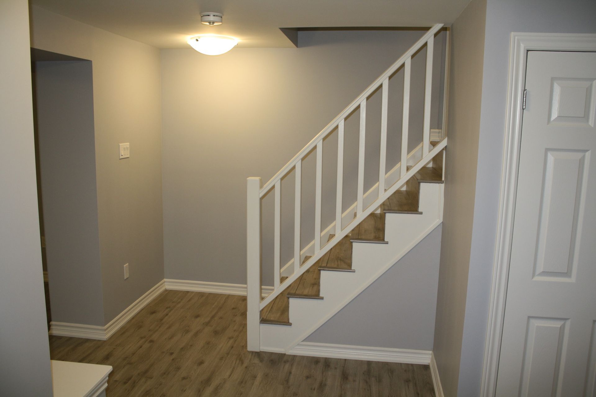Hallway with stairs and white railing, gray walls, and a white door on the right.