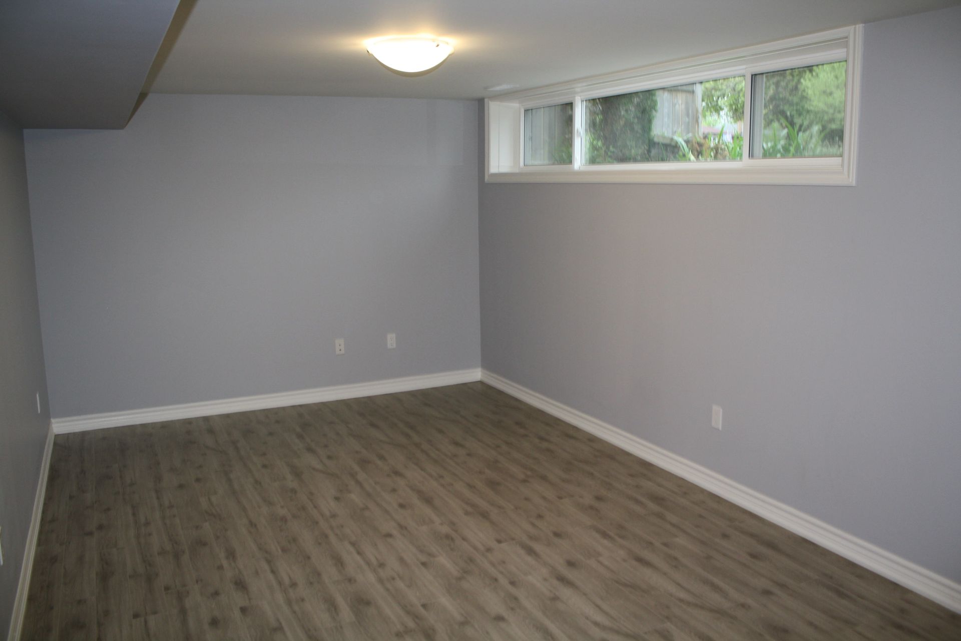 Empty room with light gray walls, wood-look flooring, and a small window.