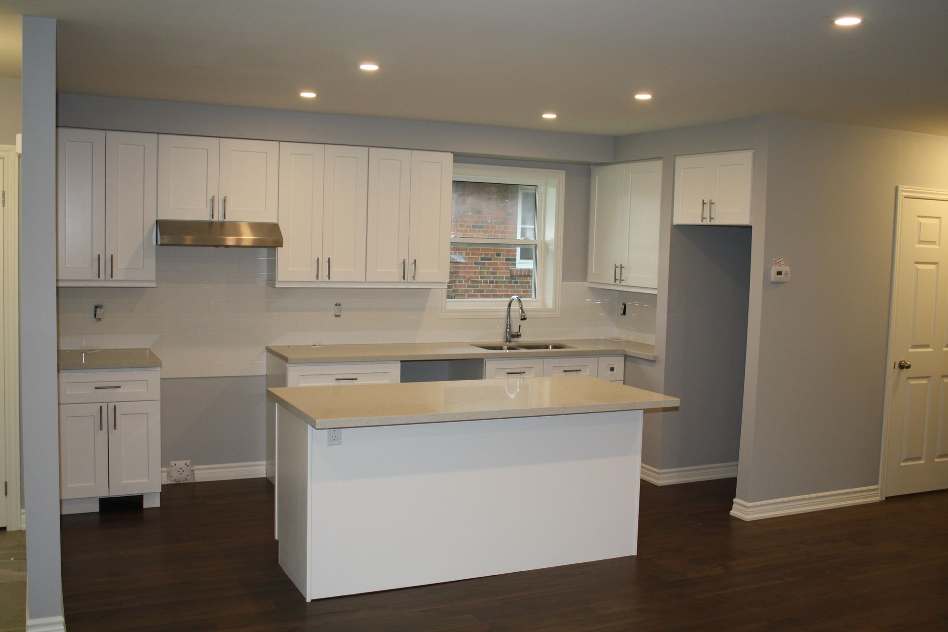 White kitchen with cabinets, island, and stainless steel hood over a sink.