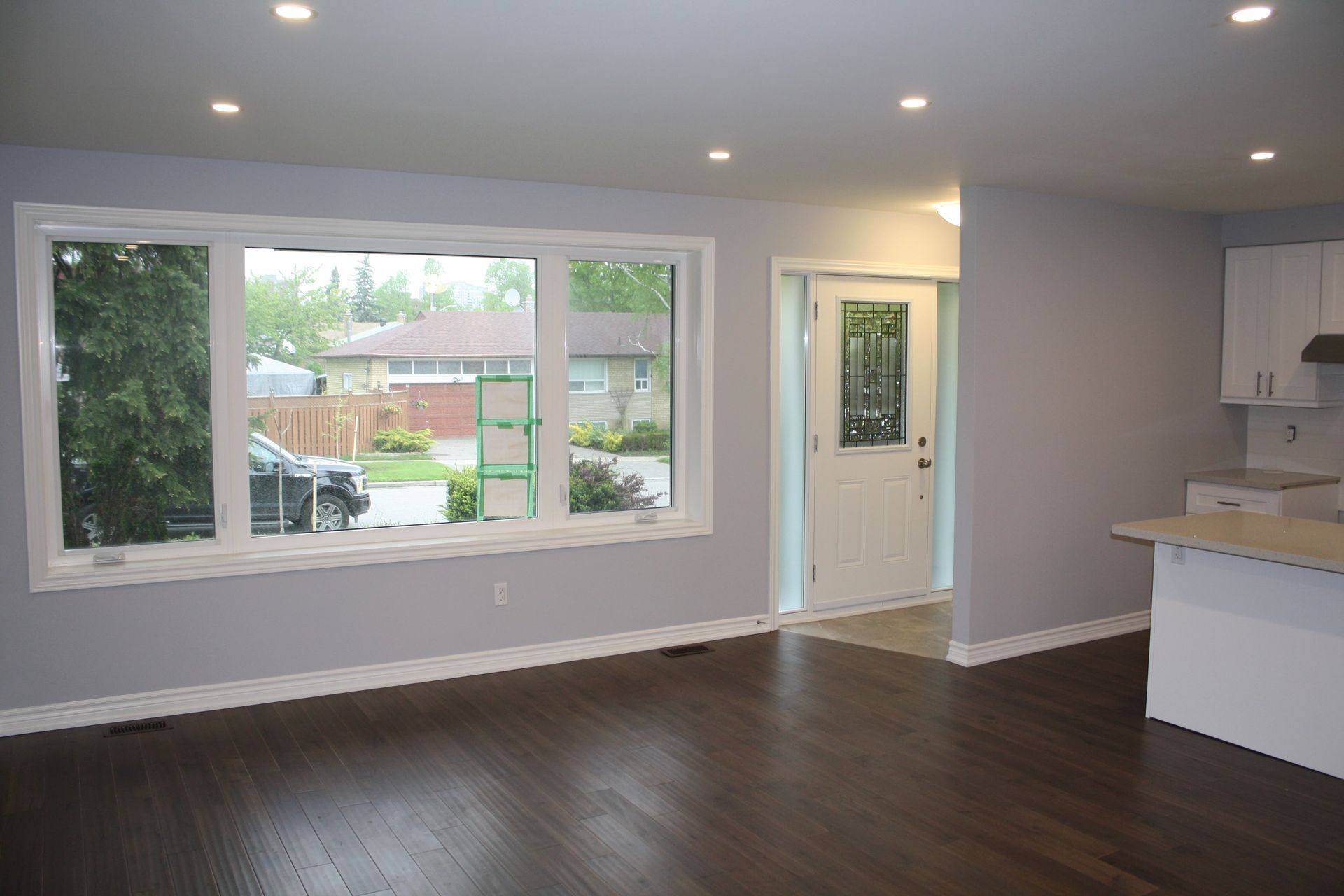 Living room with gray walls, dark wood floor, large window, white door, and recessed lighting.