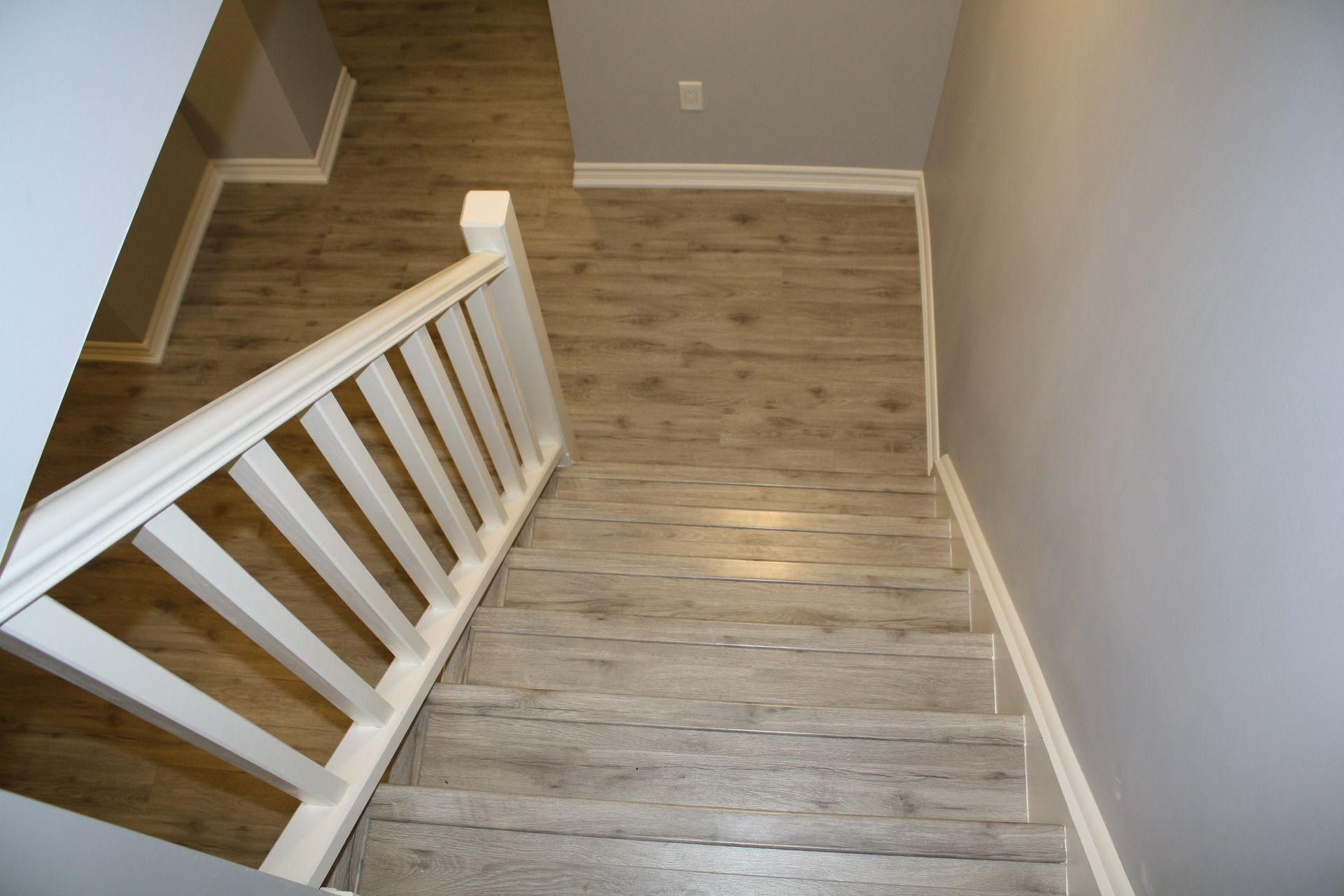 Staircase with white railing and light brown flooring, leading downward in a home with gray walls.