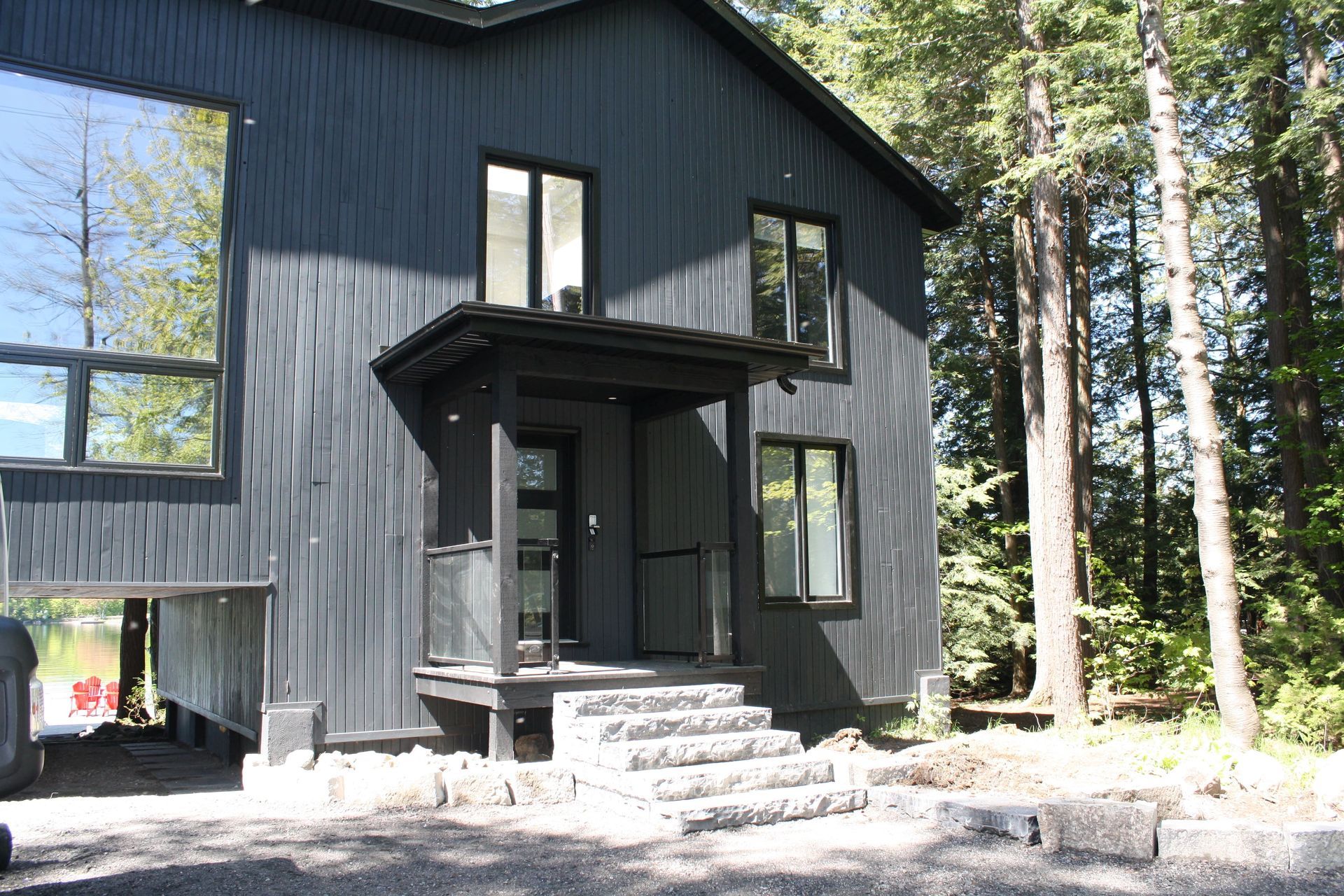 Black two-story house with several windows, porch and steps in front, surrounded by trees.