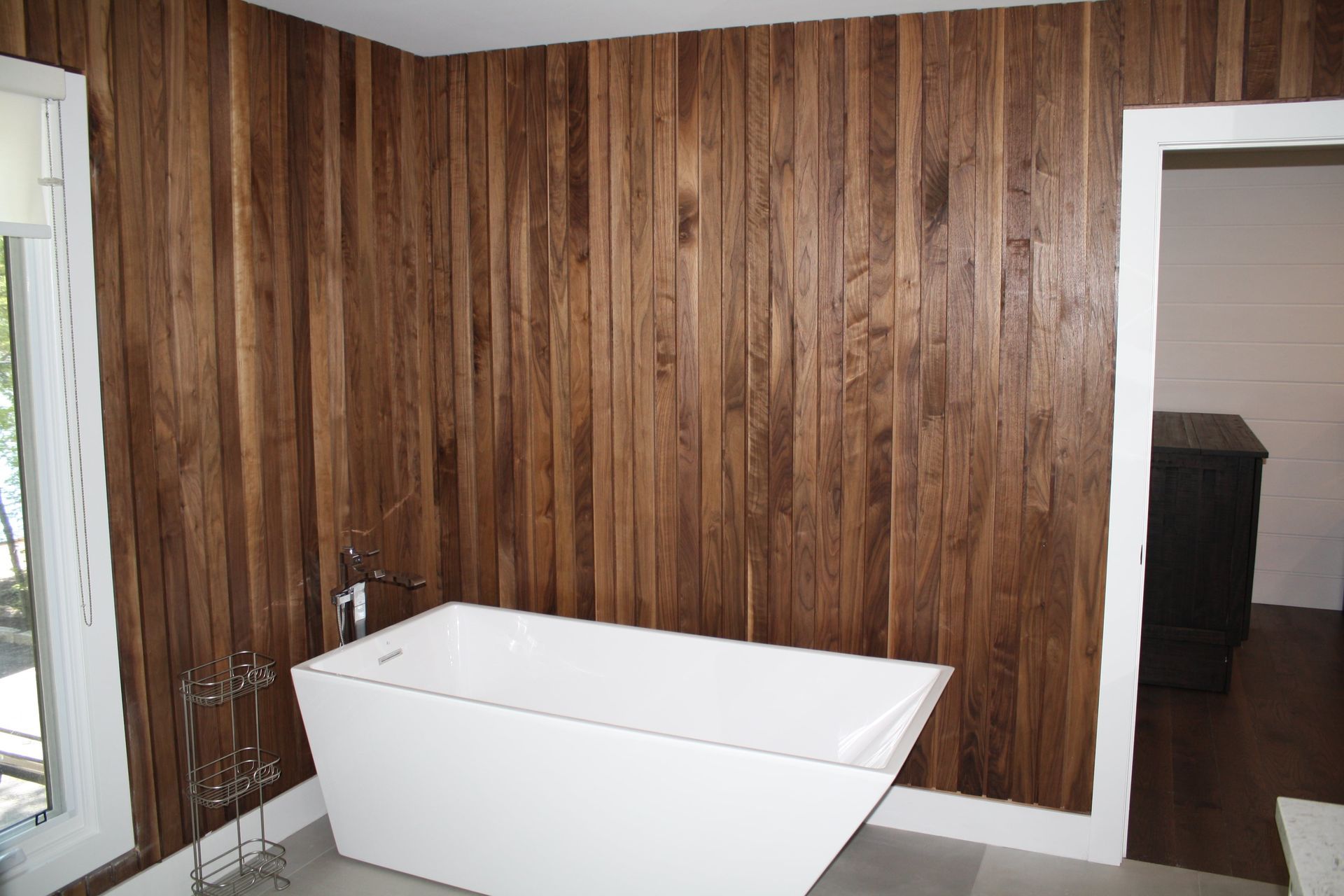 Wooden-paneled bathroom with a modern white bathtub, next to a window and doorway.