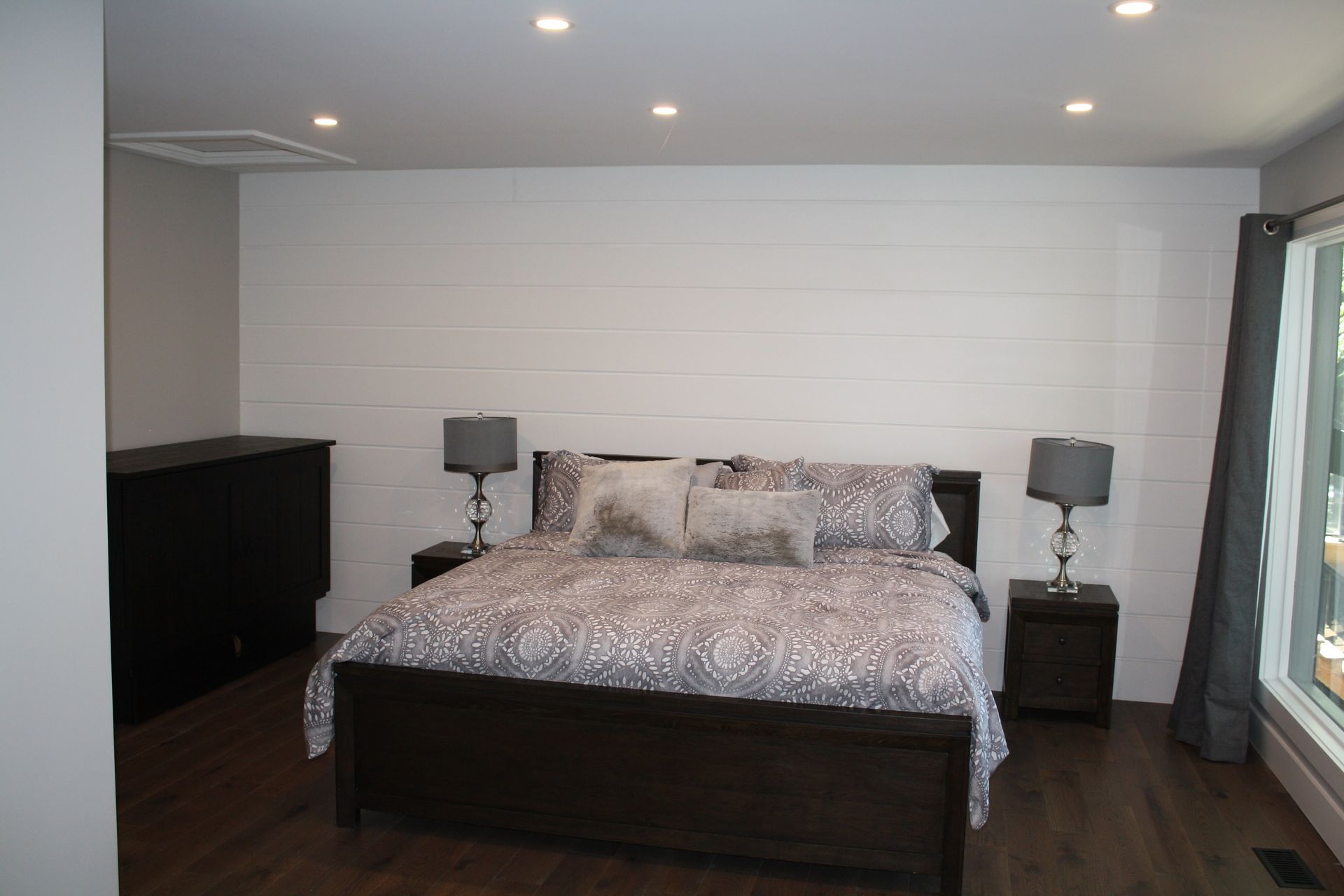Bedroom with wood plank wall, bed with patterned bedding, two nightstands, and dark wood flooring.