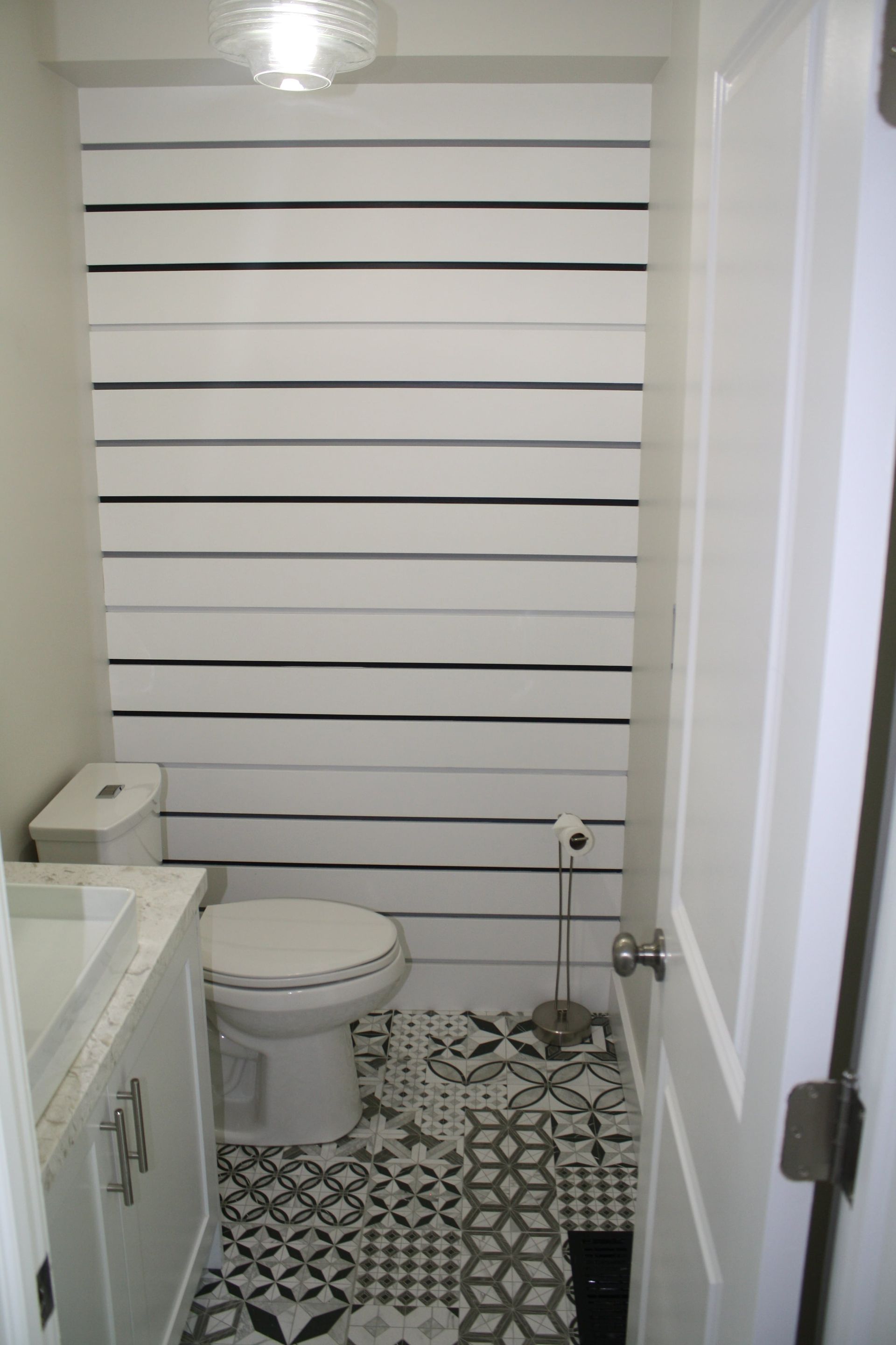 Small powder room with black and white patterned floor, white walls, and horizontal black lines on one wall.