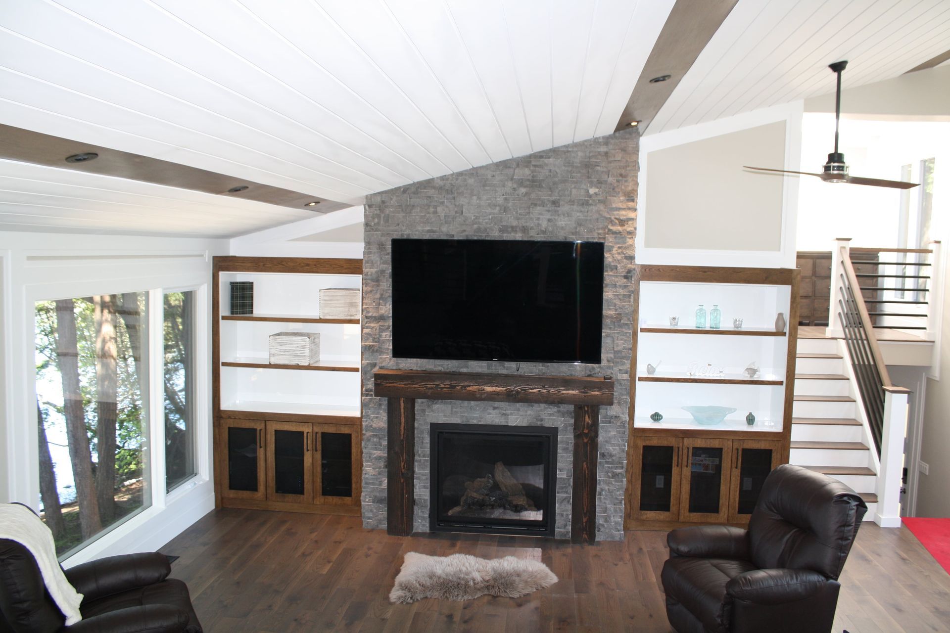 Living room with fireplace, built-in shelving, TV, dark wood floors, and a stairway.