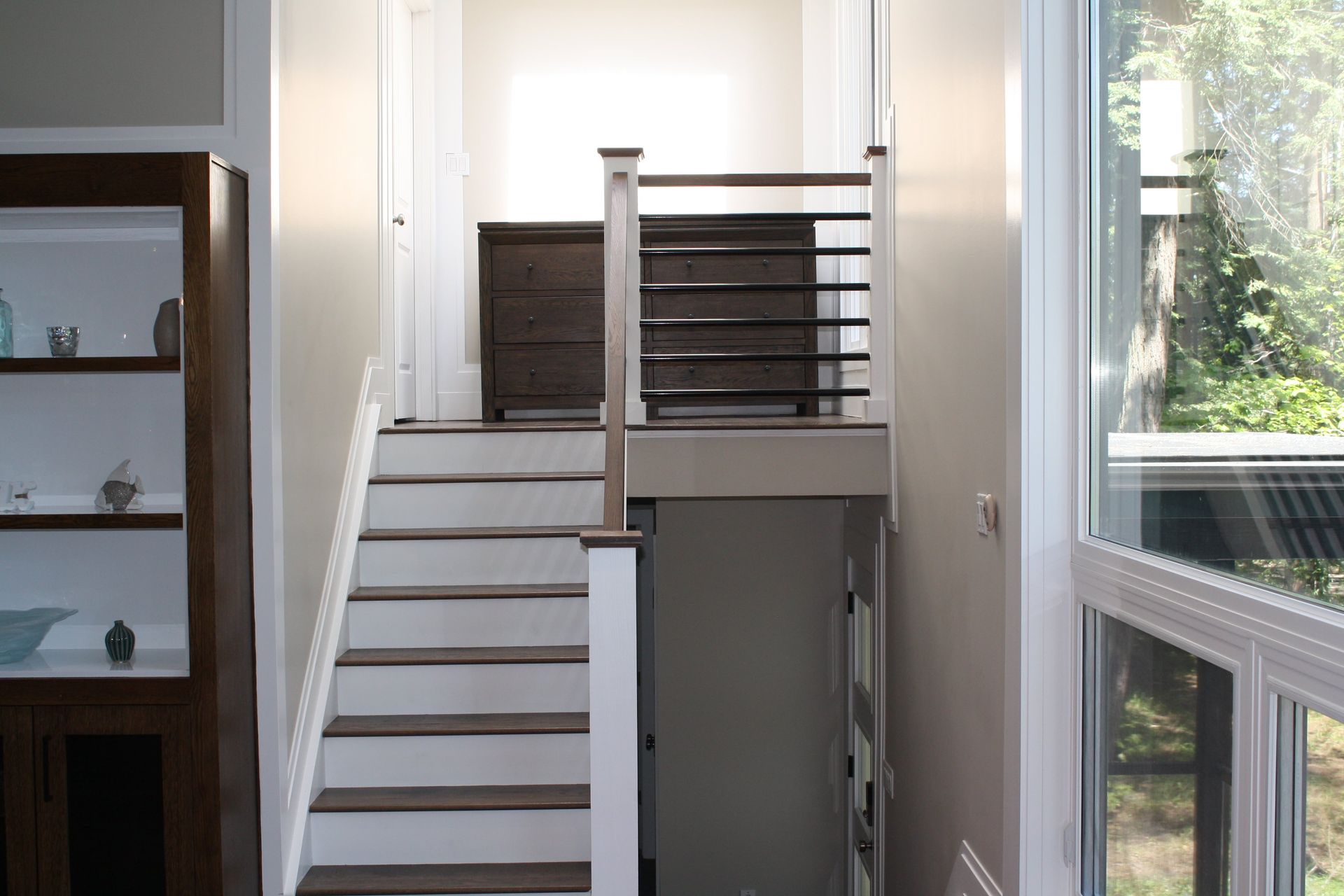 Staircase with white steps, dark wood railing, and doorway at the top, leading down to a basement.