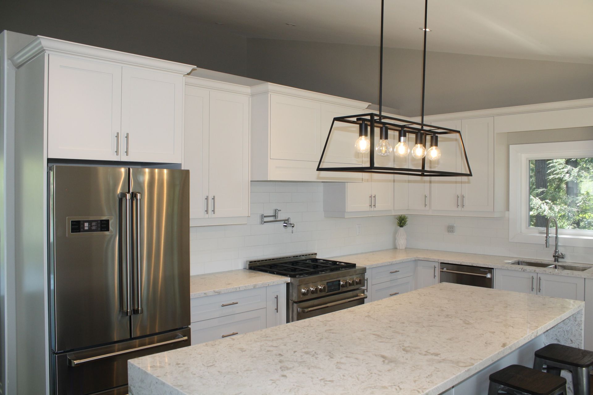 White kitchen with stainless steel appliances, countertop island, and geometric light fixture.