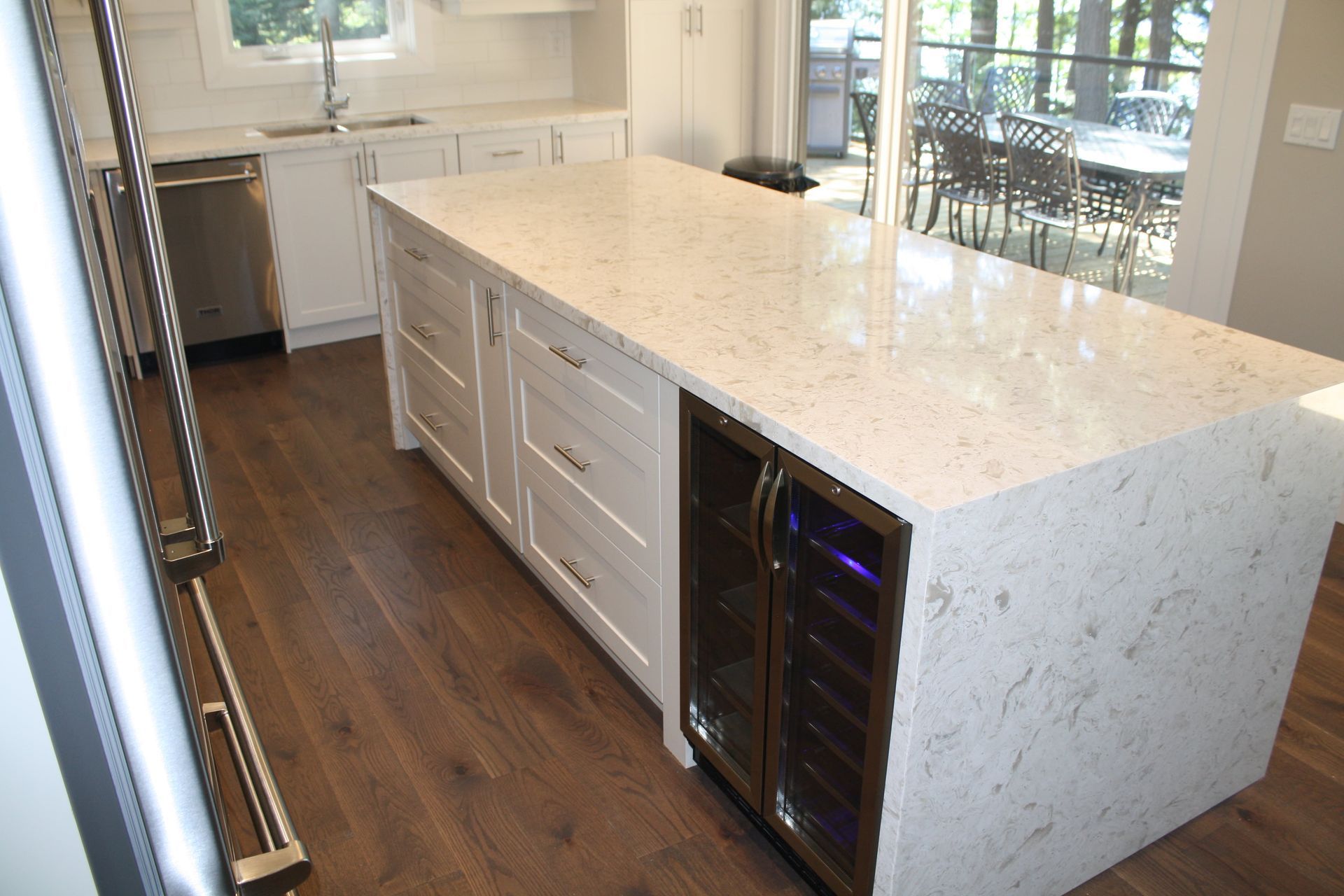 White kitchen island with a stone countertop and wine cooler on hardwood floor.