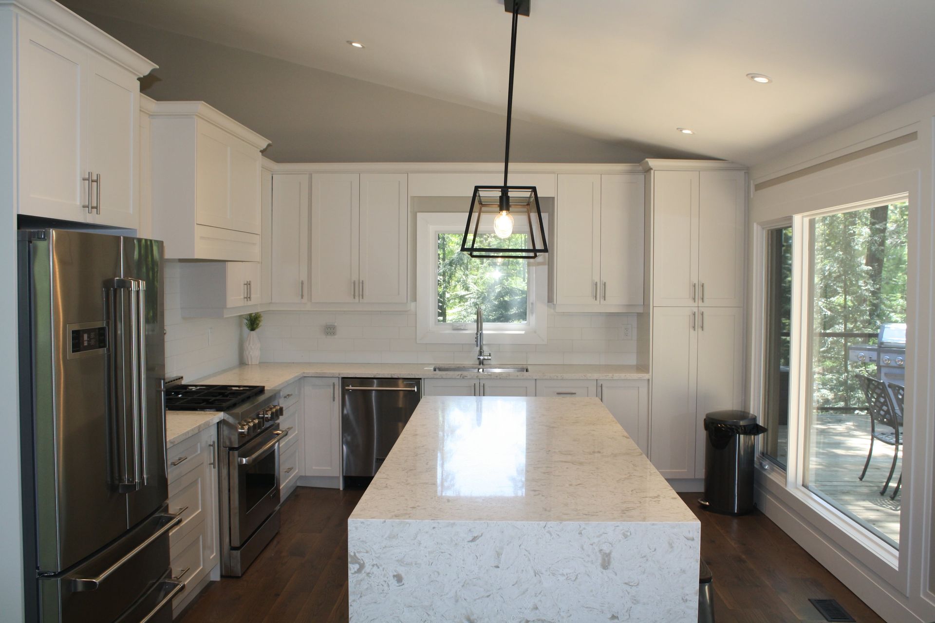 White kitchen with island, stainless steel appliances, and window overlooking trees.