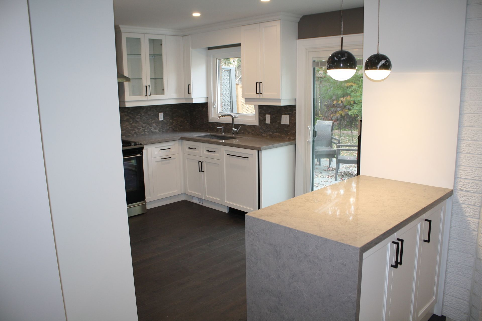 White kitchen with dark countertops, cabinets, and flooring; view of a patio through a sliding glass door.