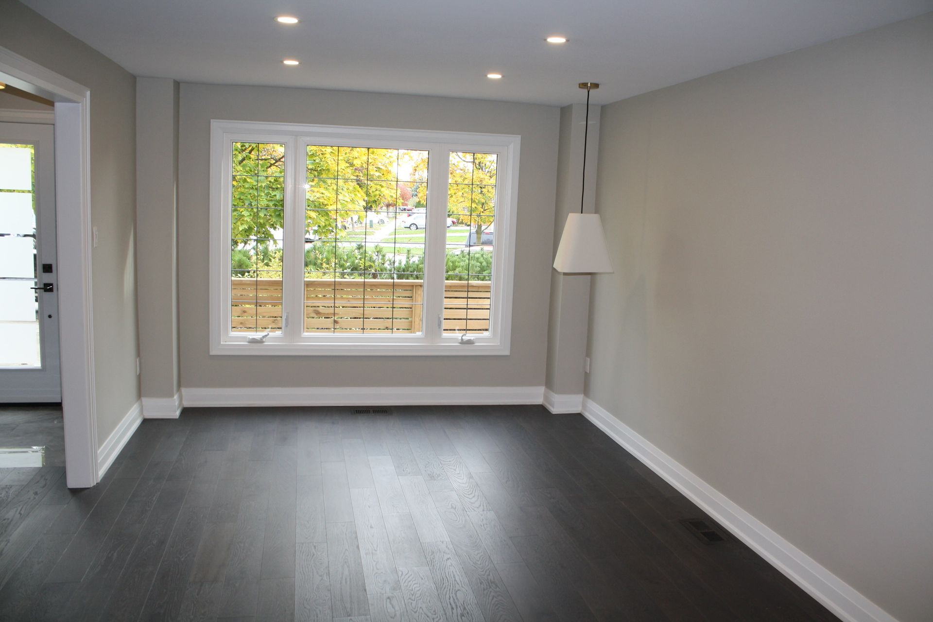 Empty room with dark hardwood floor, large window, and recessed lighting.
