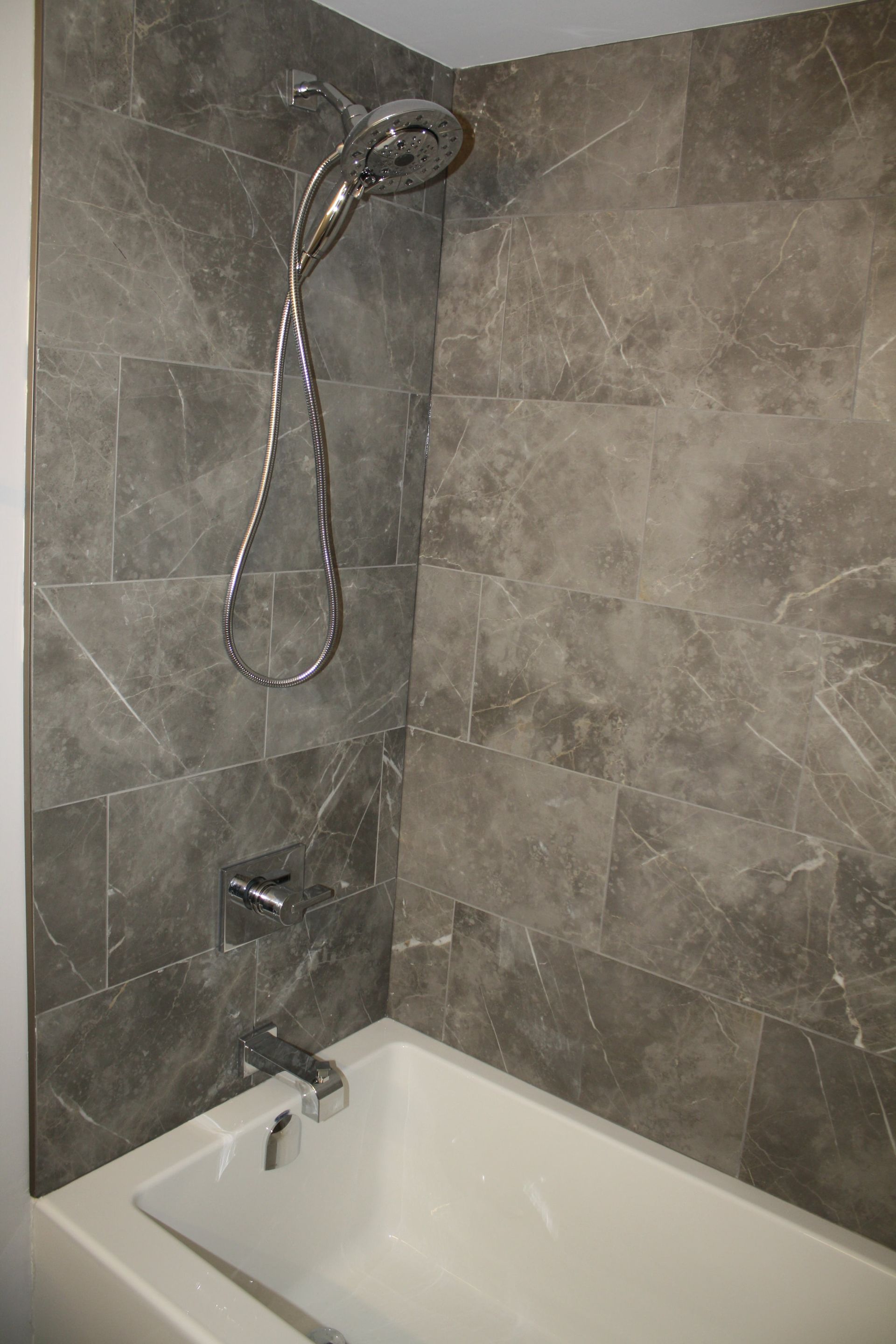 A shower and bathtub combination with gray tile walls and chrome fixtures.