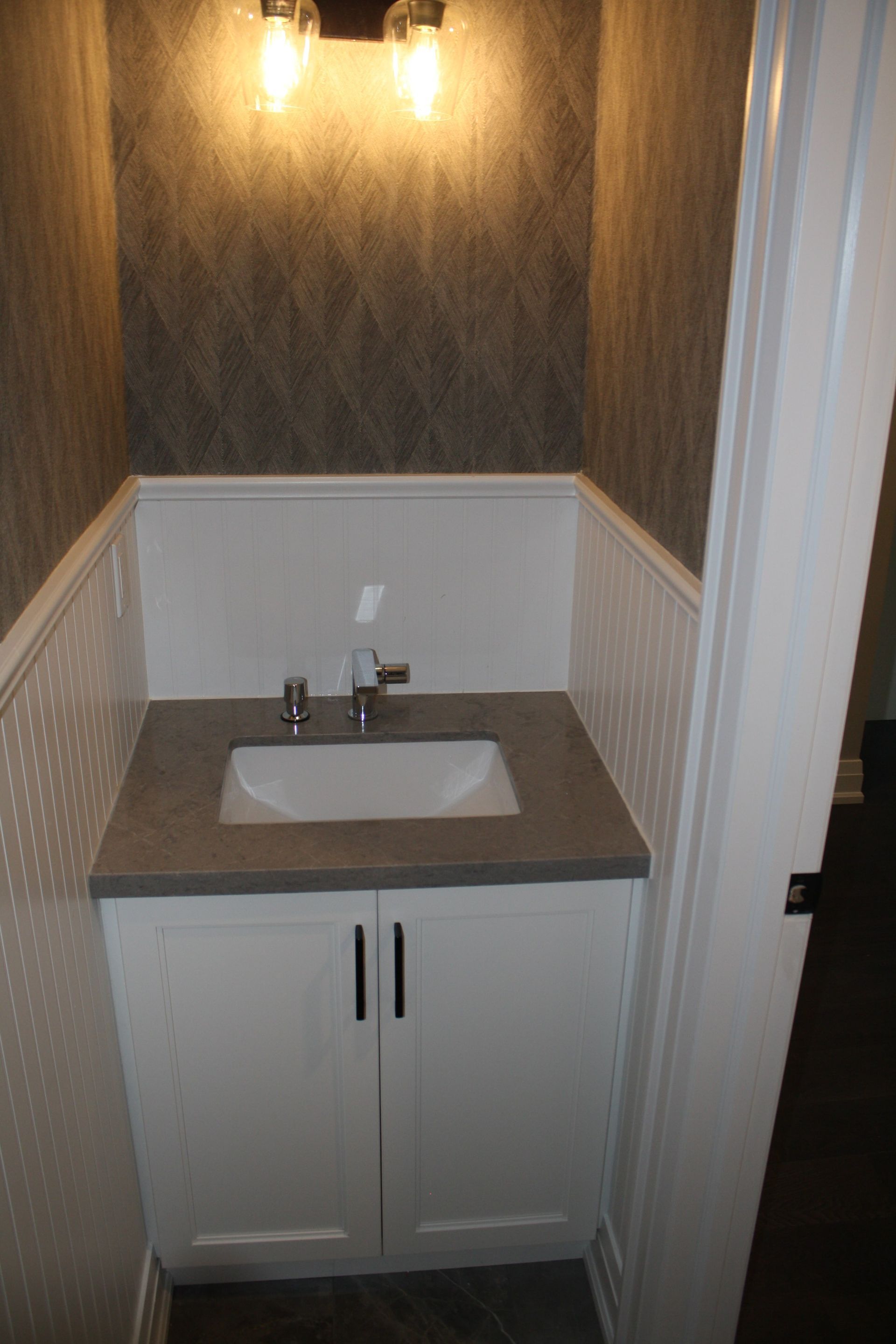 Small white powder room with a white cabinet, sink, and textured wallpaper.