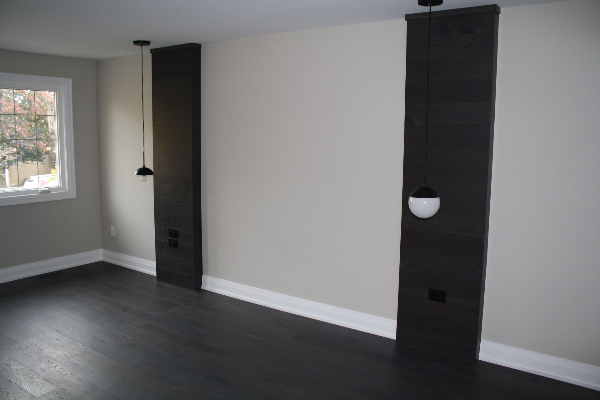 Dark wood panel accent walls with hanging pendant lights in a room with dark wood flooring.
