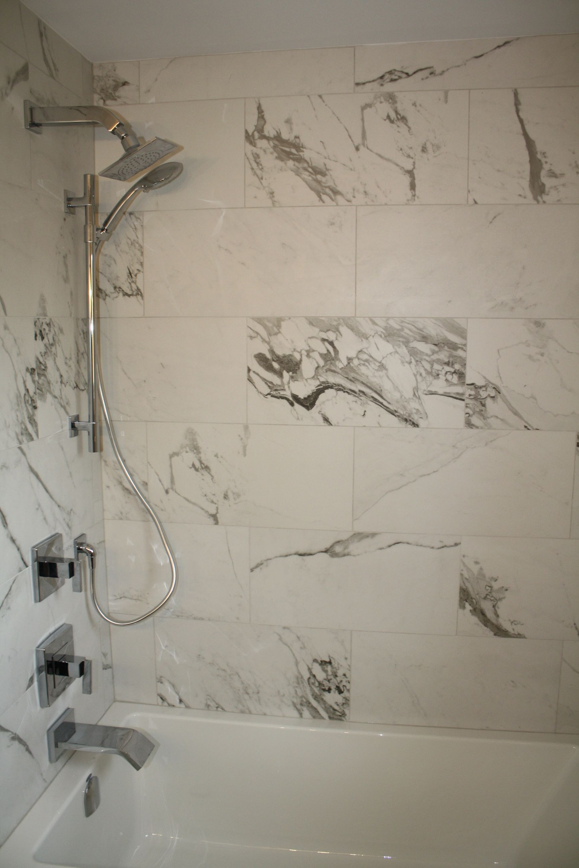 Marble-tiled shower with silver showerhead and faucet, above a white bathtub.