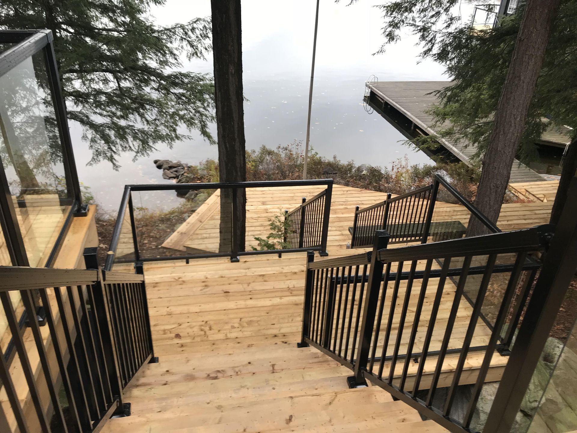 Wooden stairs with black railings lead to a deck overlooking water.