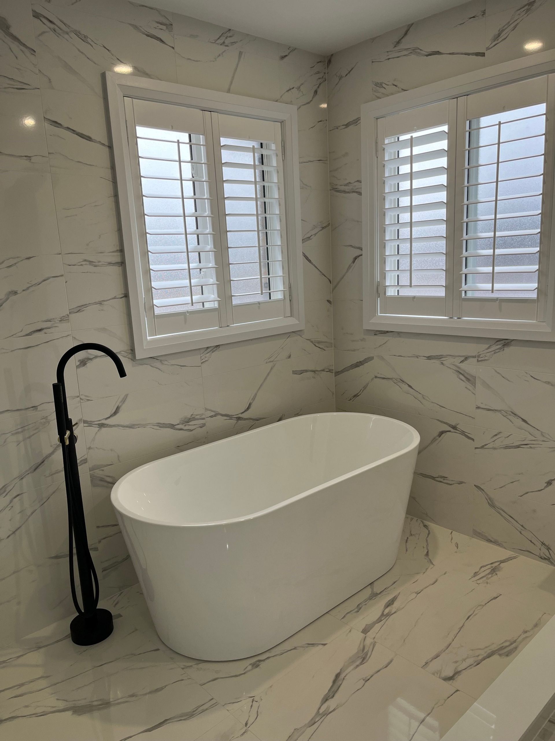 Modern bathroom with a white freestanding bathtub, black faucet, and marble-look tile.
