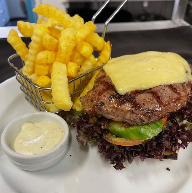 Steak burger with fries and dipping sauce on a white plate.