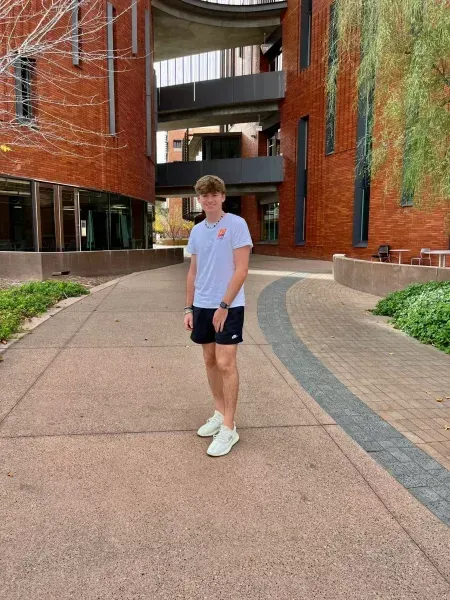 Person standing on a curved walkway between red brick buildings and greenery.