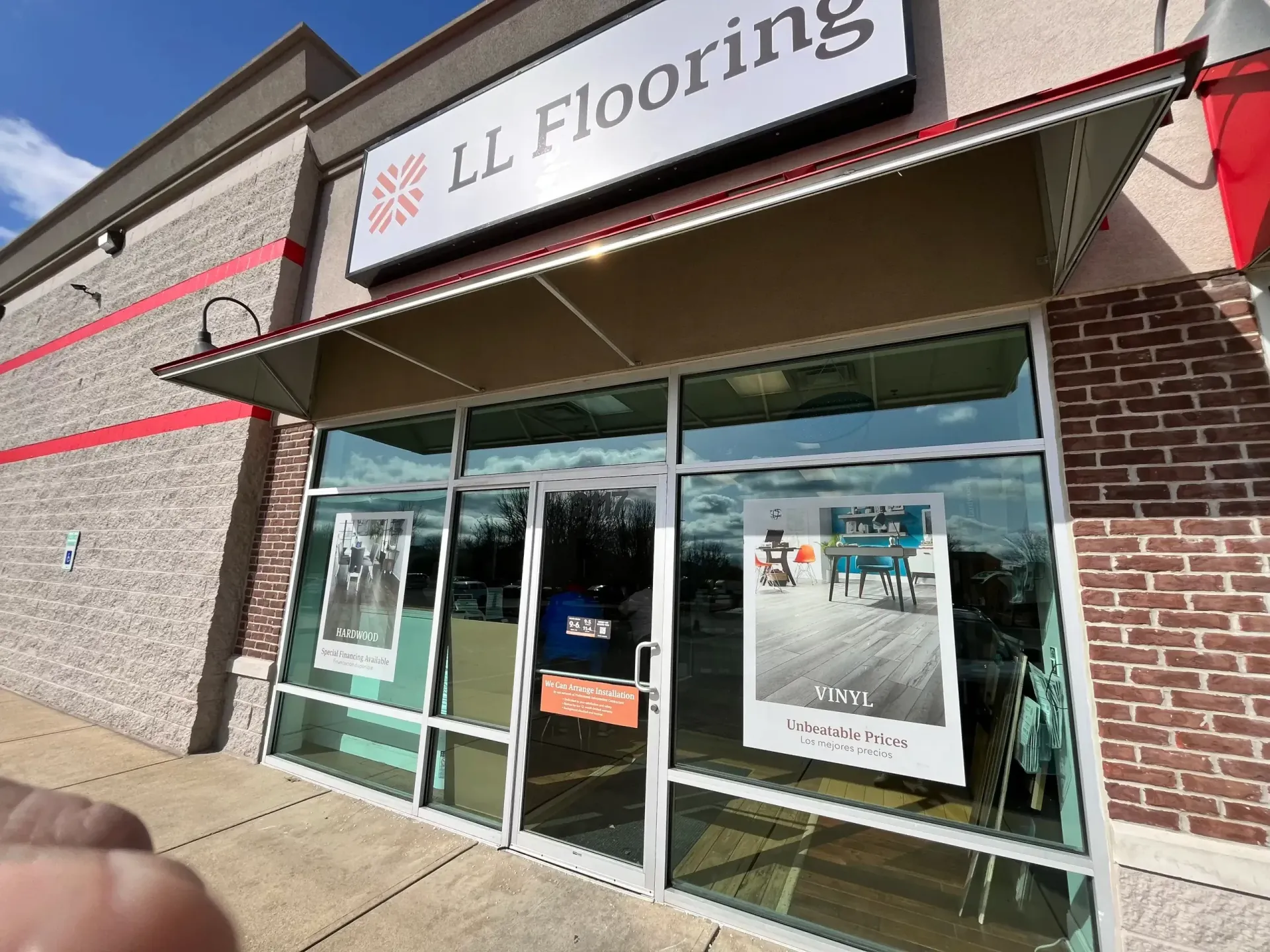 LL Flooring storefront with glass entrance and red awnings on a sunny day