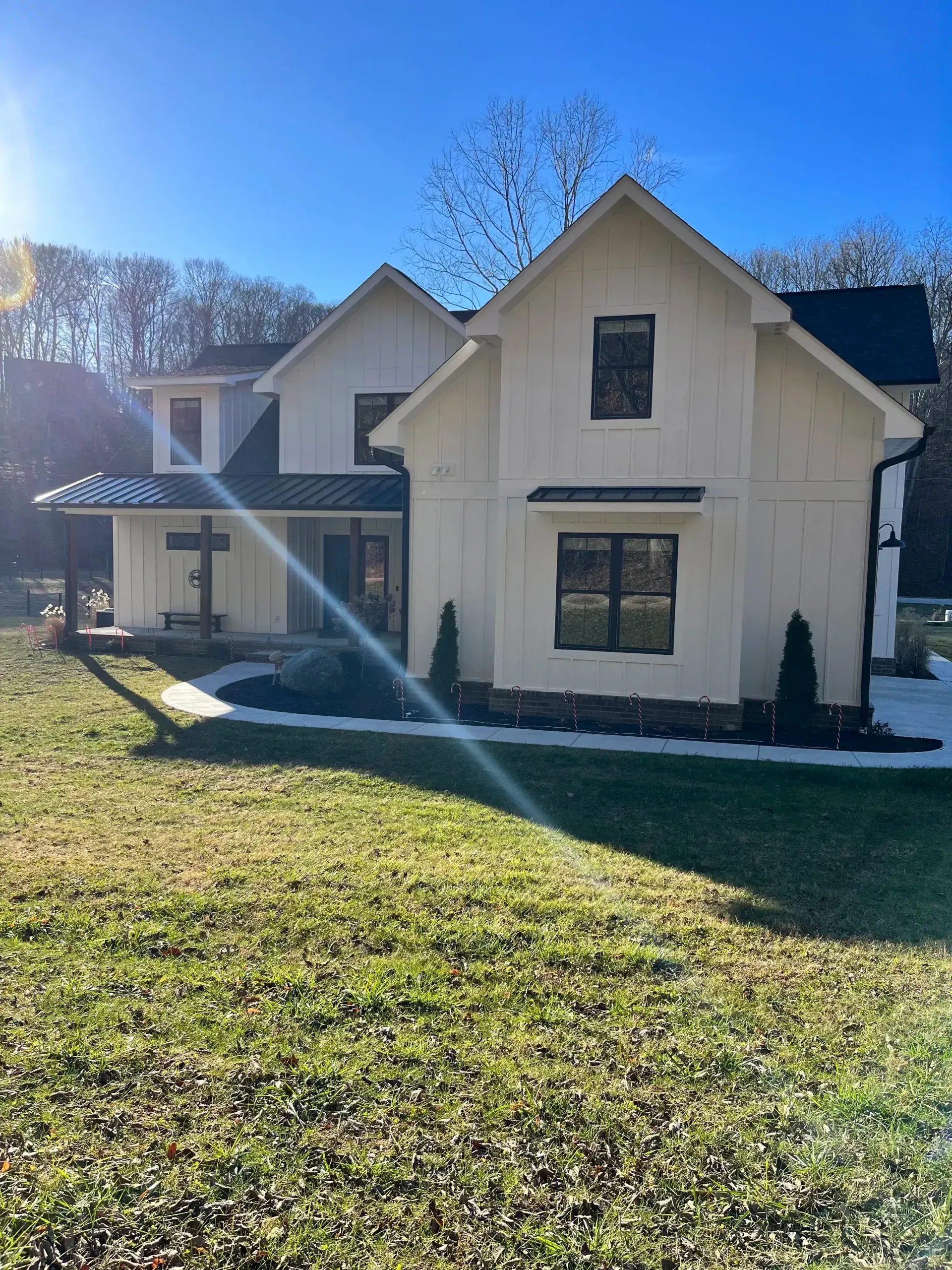 Two-story cream house with a front porch and large lawn in bright sunlight